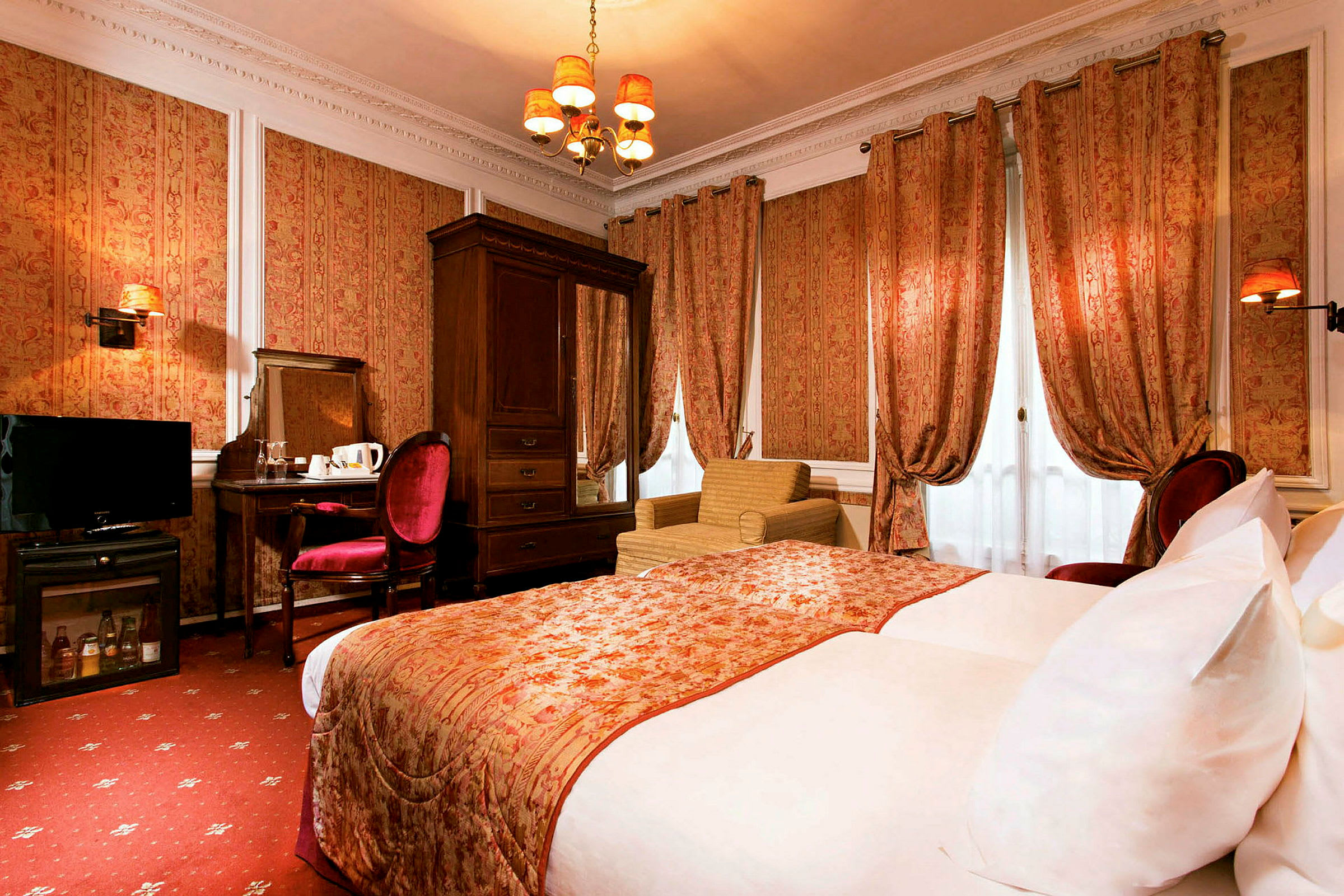 Et klassisk innredet hotellrom med en stor seng, gardiner, lenestol og et skrivebord med stol. (AI-generert tekst)