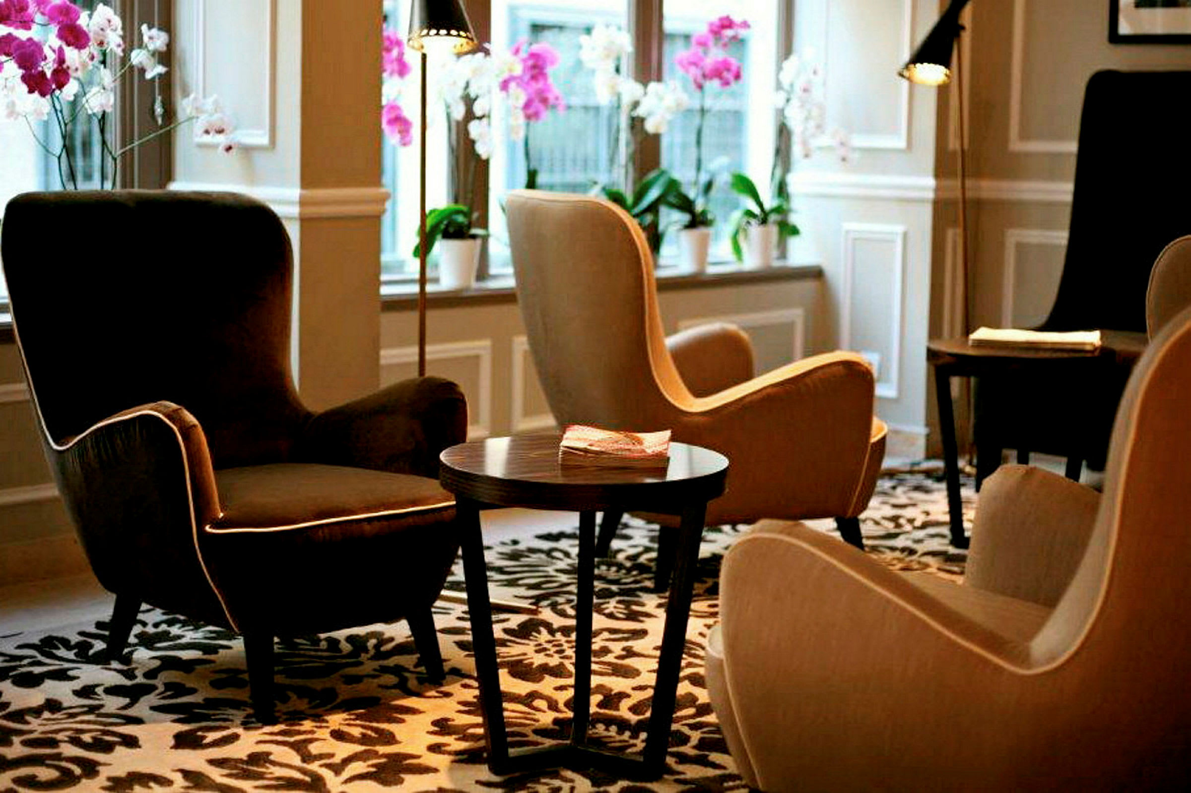 En lounge med komfortable lenestoler, et bord og dekorative blomster i vinduene. (AI-generert tekst)