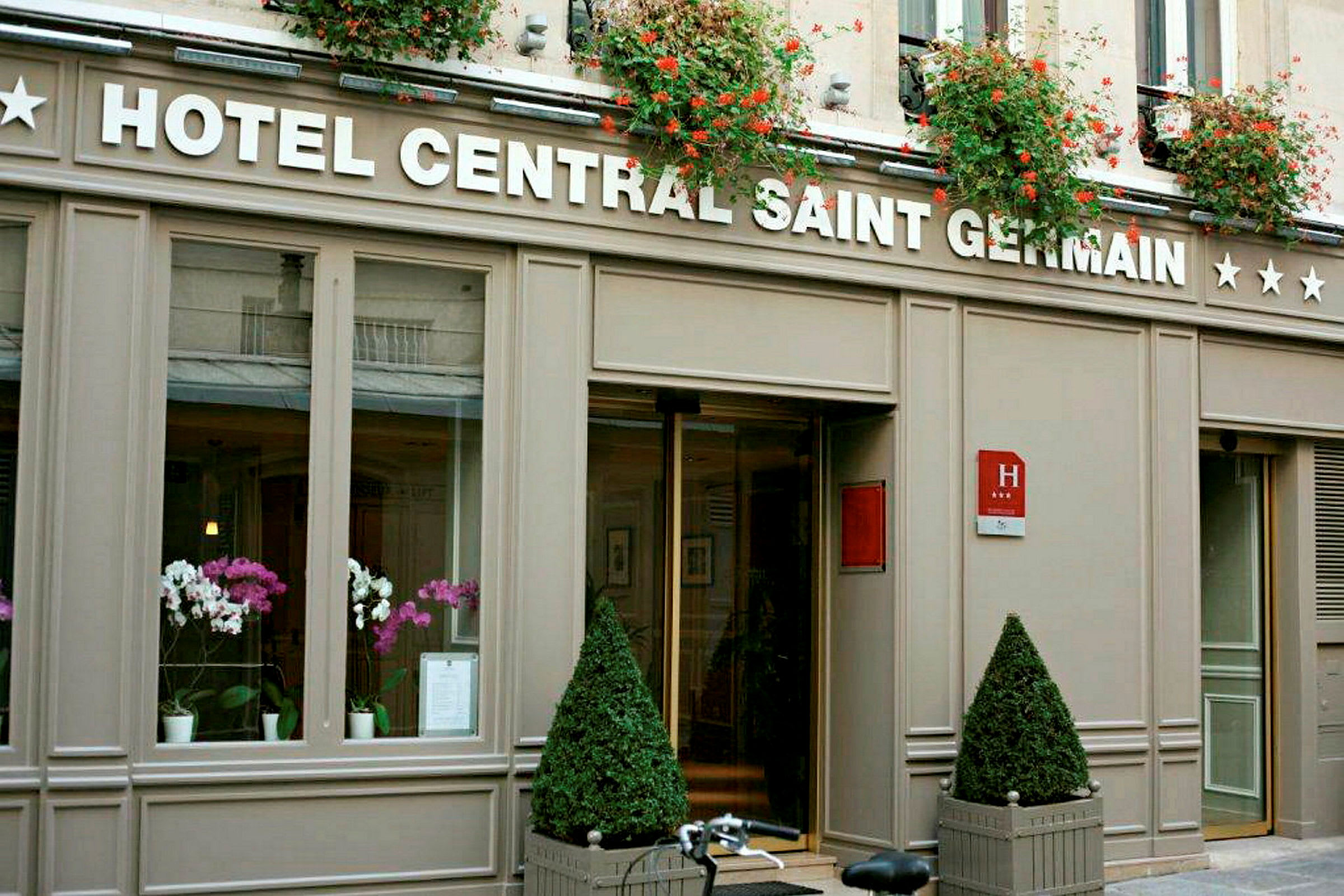 Bilde av hotellinngangen til Hotel Central Saint Germain med blomsterdekorasjoner og skiltet synlig. (AI-generert tekst)