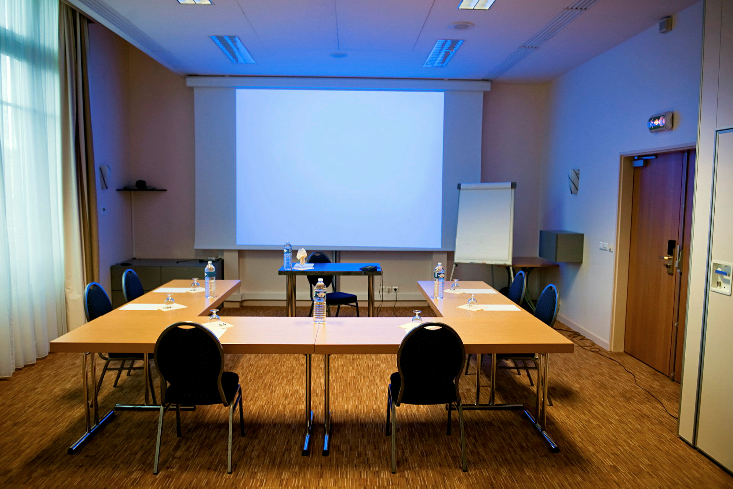 Et konferanserom med en oppsatt presentasjonsskjerm, bord ordnet i en u-form og stoler plassert rundt. (AI-generert tekst)
