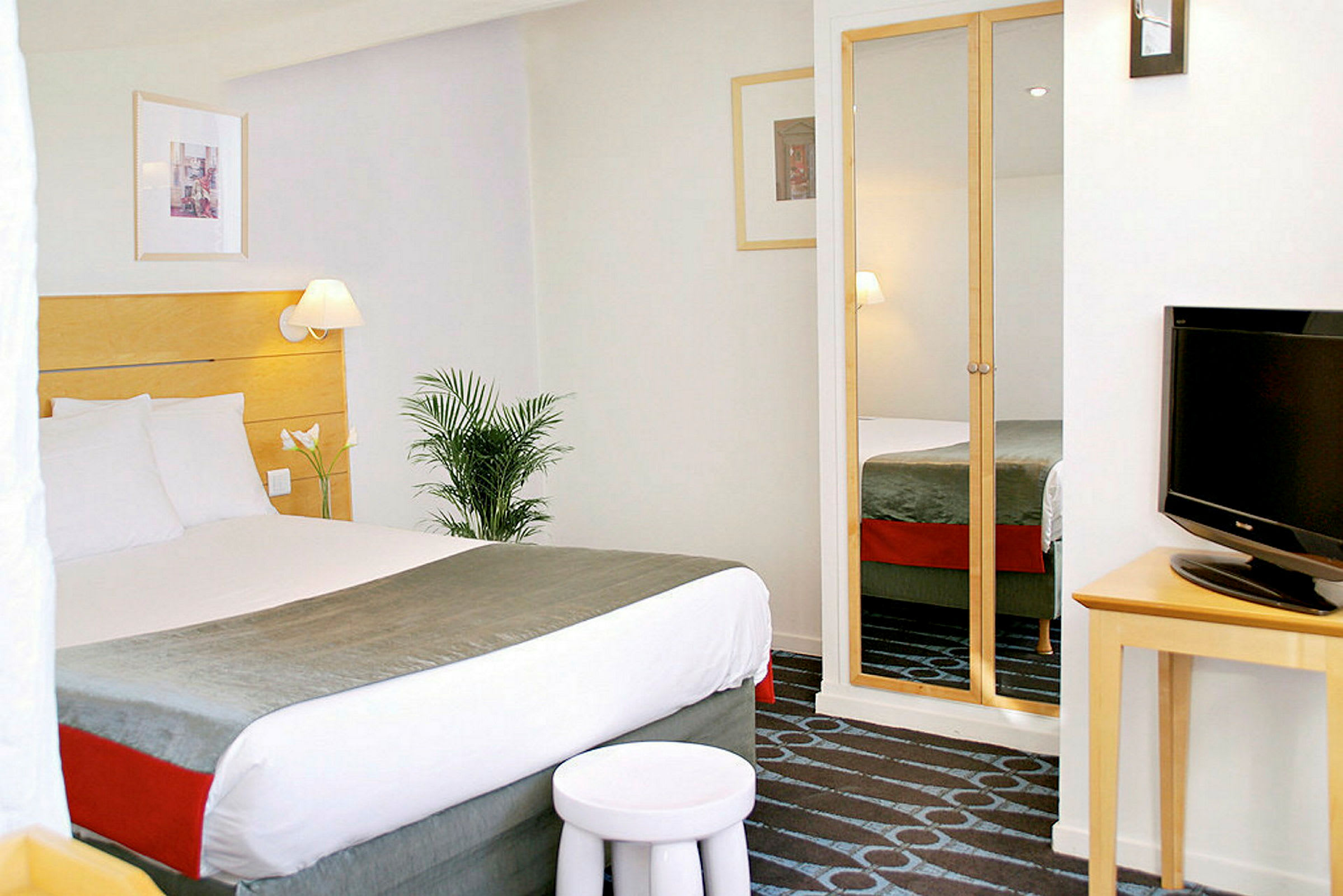 Hotellrom med en oppredd dobbeltseng, TV og speildør garderobe. (AI-generert tekst)