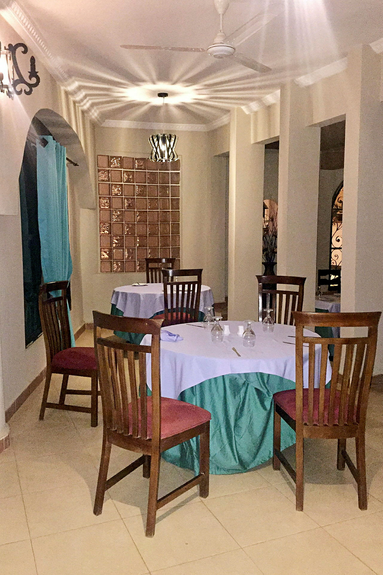 En restaurant med bord dekket med hvite og grønne duker, omgitt av trestoler. (AI-generert tekst)