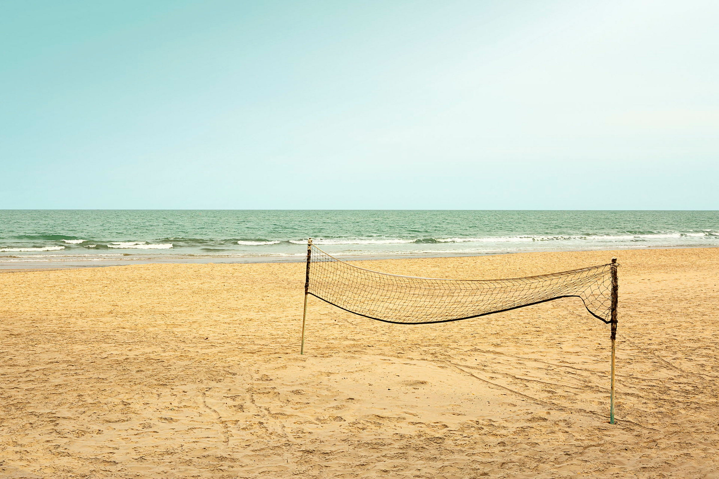 En tom sandstrand med et oppsatt volleyballnett og havet i bakgrunnen. (AI-generert tekst)