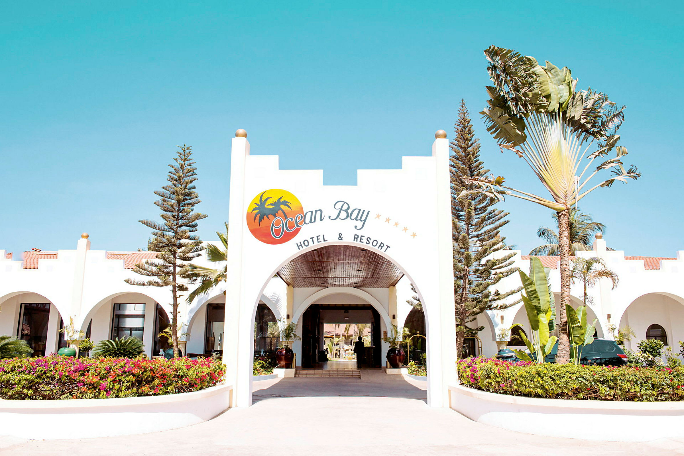 Inngangen til Ocean Bay Hotel & Resort, med en buet åpning og omkringliggende beplantning. (AI-generert tekst)