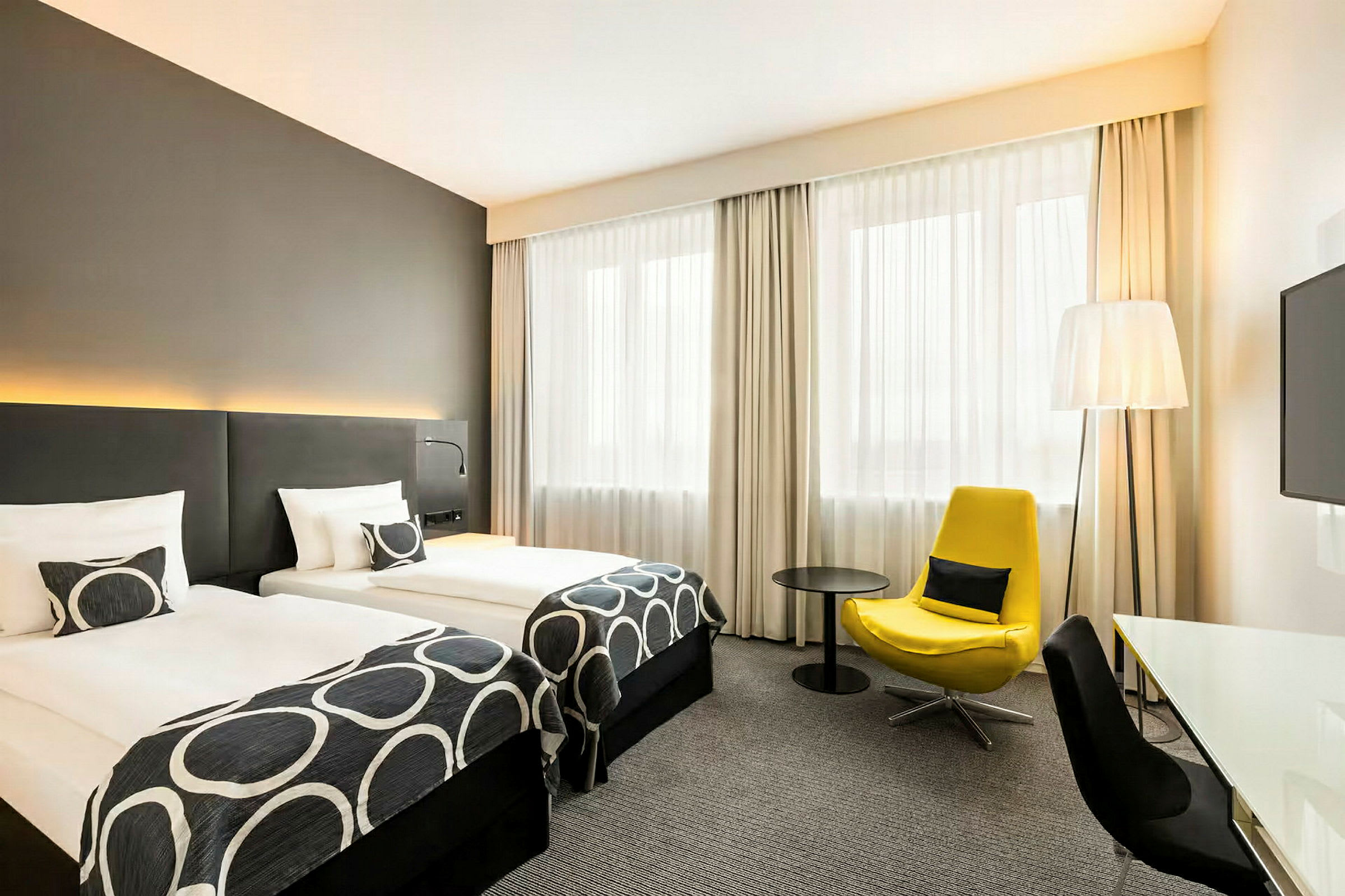 Et hotellrom med to enkeltsenger, en gul lenestol og et skrivebord. (AI-generert tekst)