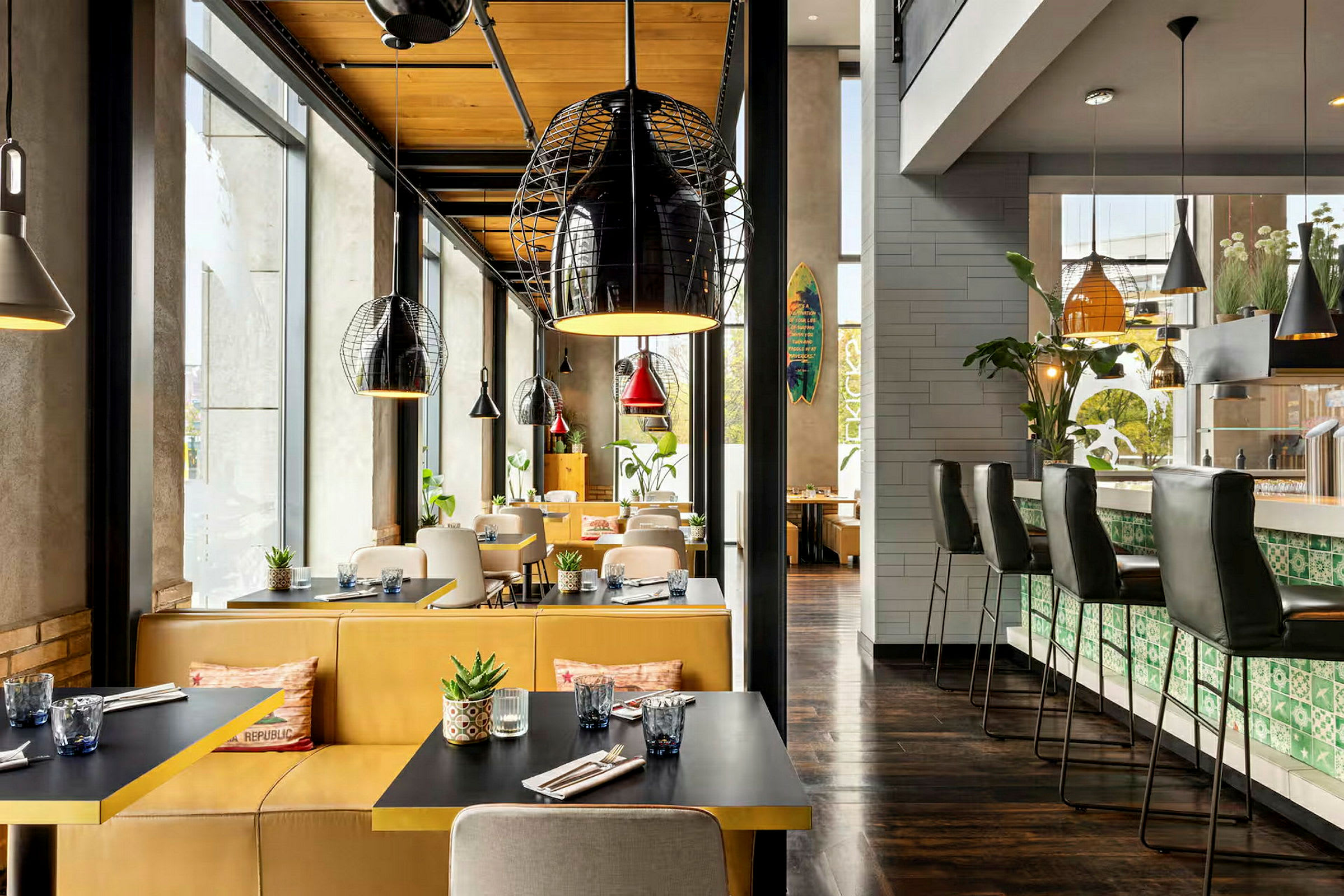 Interiør av en restaurant med sitteplasser ved bord og en bardisk, dekorert med moderne lamper og planter. (AI-generert tekst)