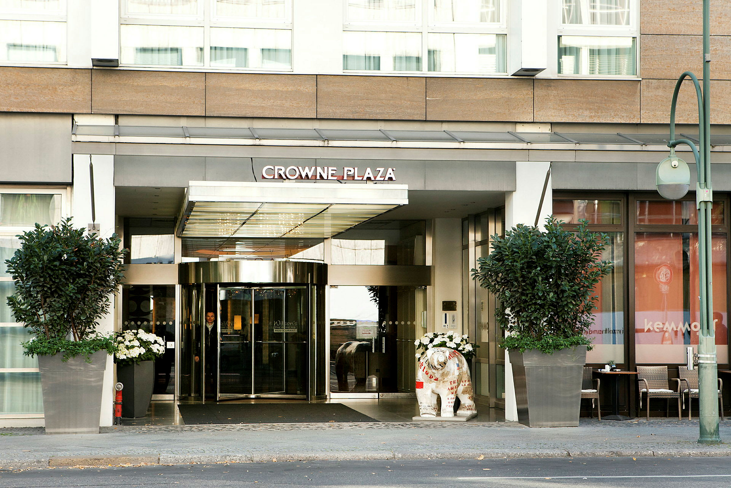 Inngangen til hotell Crowne Plaza med glassdører og store blomsterpotter. (AI-generert tekst)