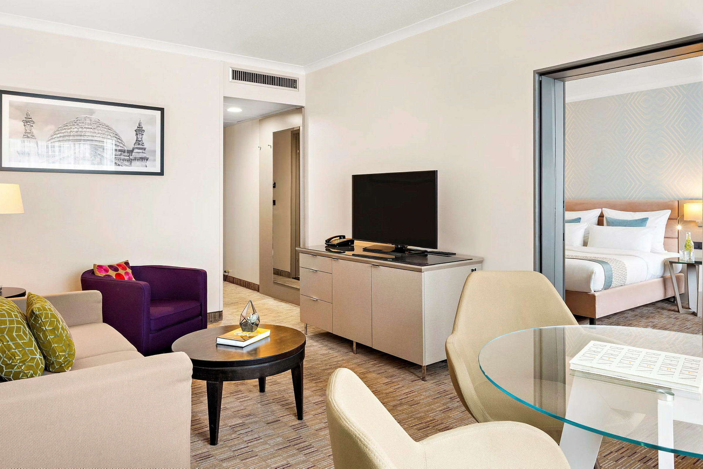 Stue i en hotellsuite med sittemøbler, TV og åpning til soverom. (AI-generert tekst)