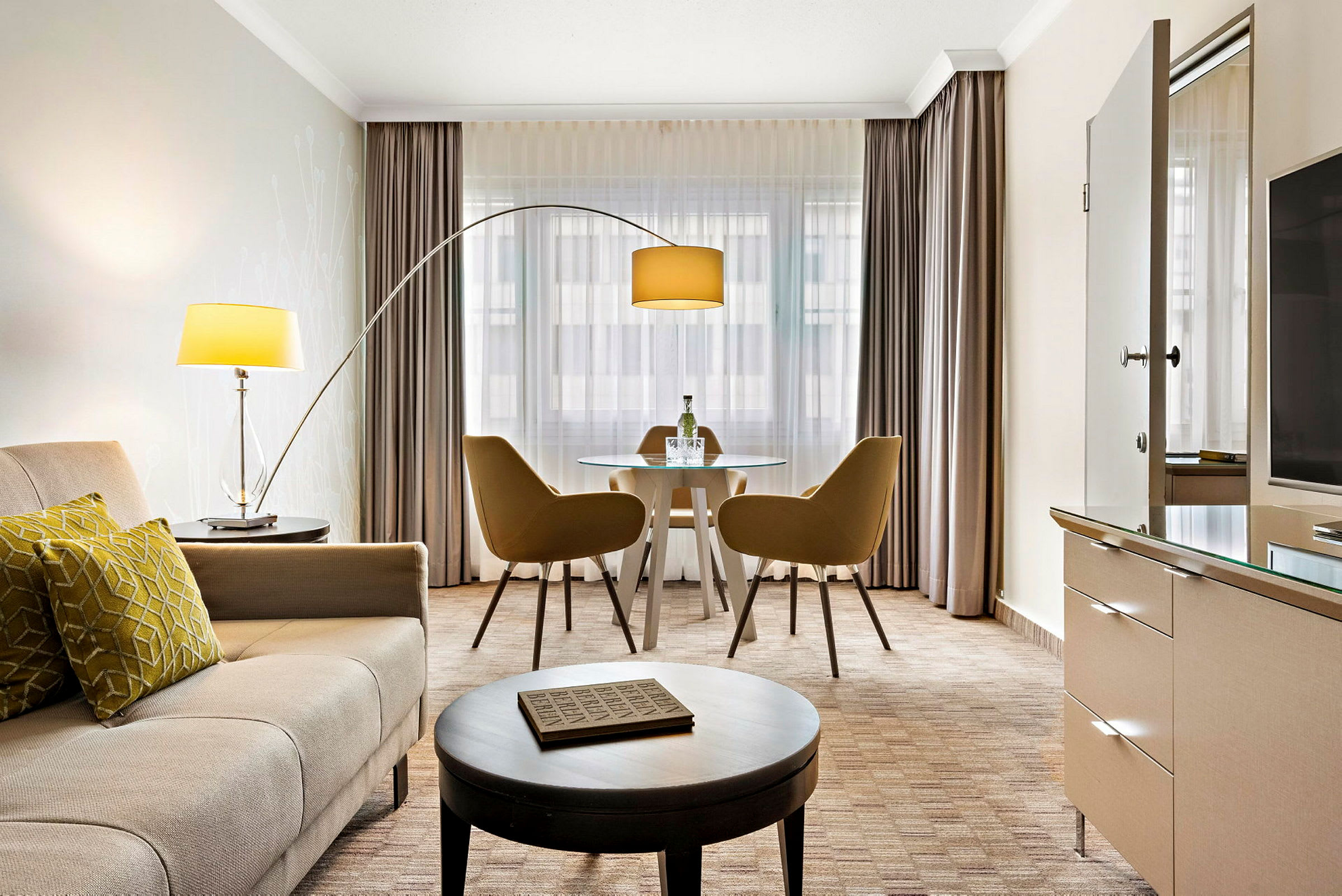 Et moderne hotellrom med sittegruppe, bord med to stoler, sofa og lamper. (AI-generert tekst)