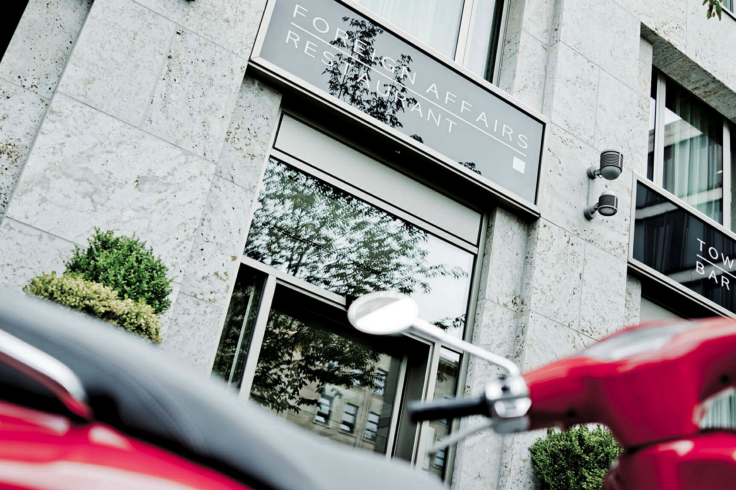 En moderne bygning med skilt for en restaurant og en bar, hvor en rød scooter er i forgrunnen. (AI-generert tekst)