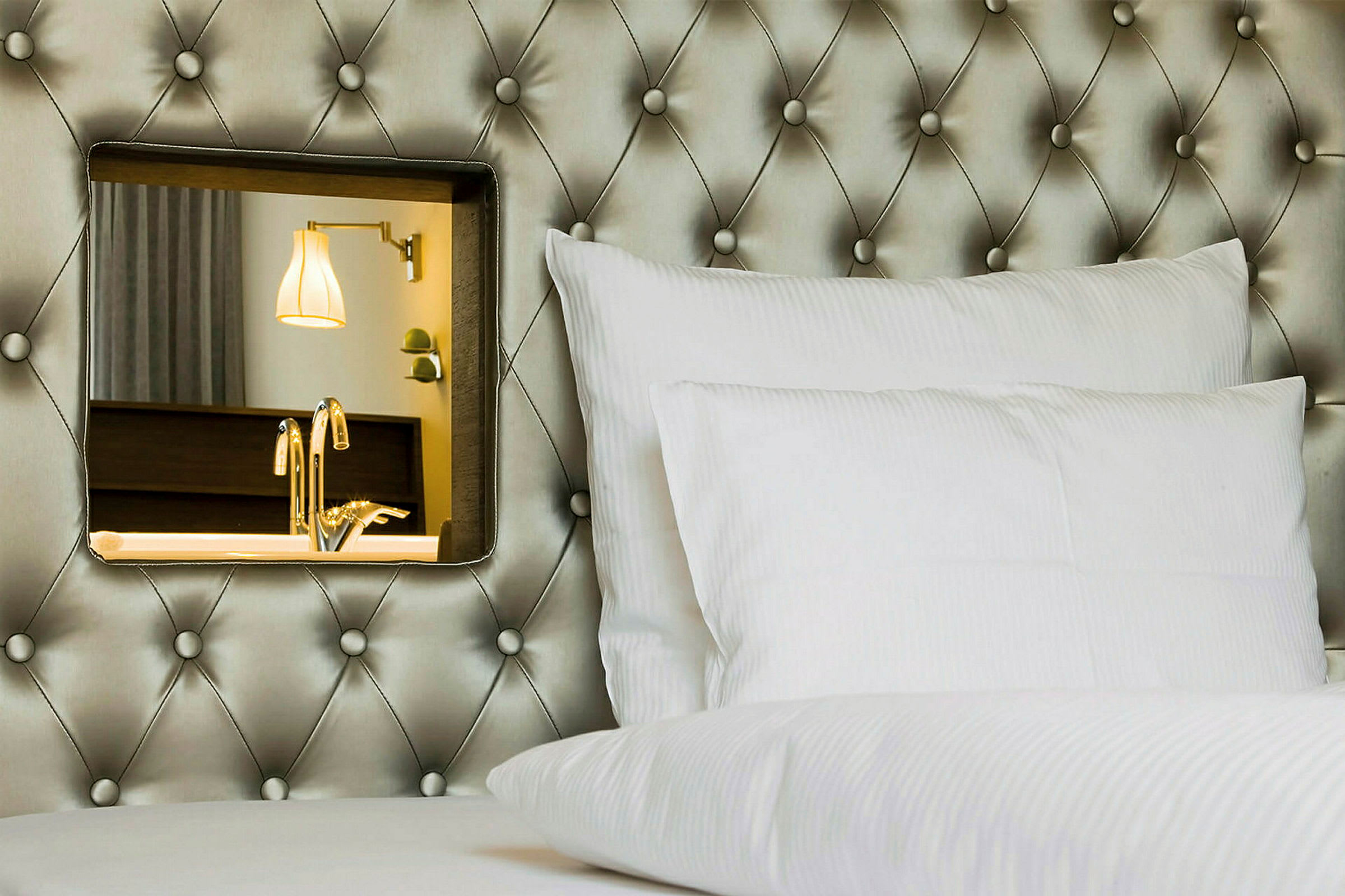 Hotellseng med hvit pute og dekorativ speil på den polstrede sengegavlen. (AI-generert tekst)