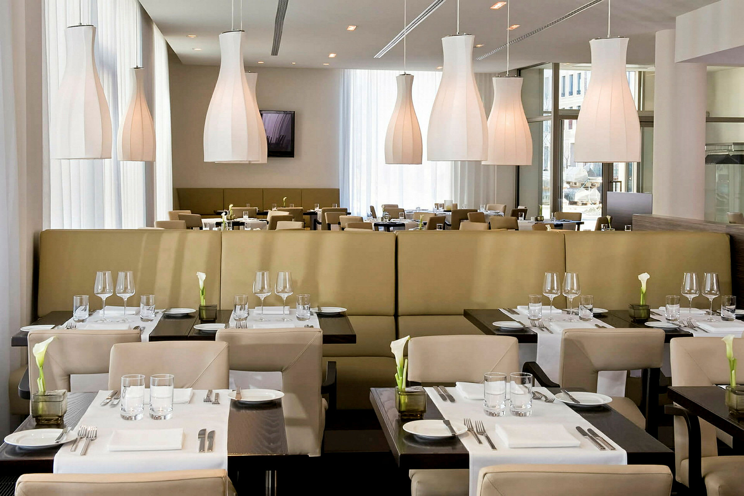 En restaurant med moderne møbler og dekket bord. Lyse hengende lamper vises i taket. (AI-generert tekst)