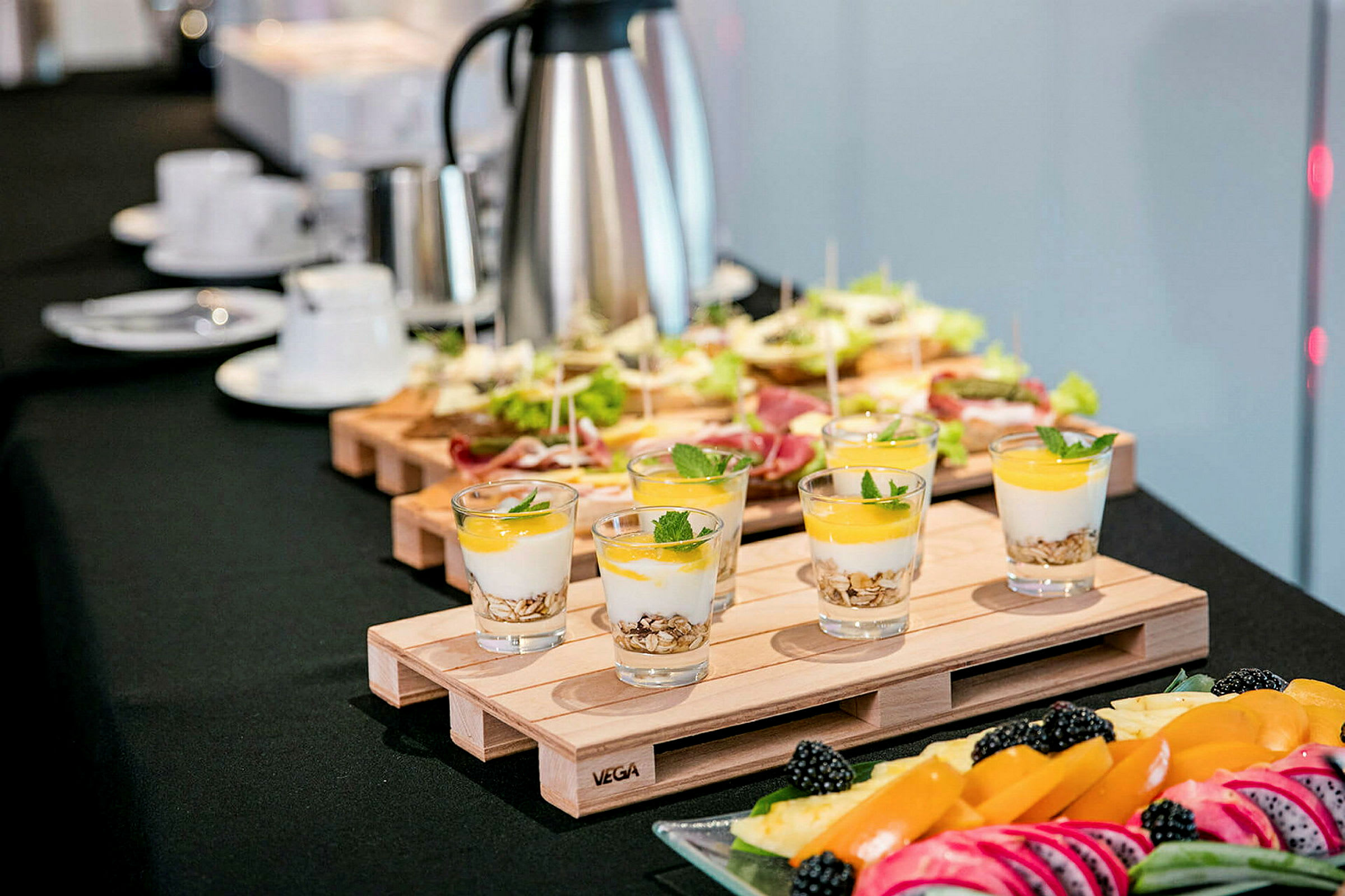 Et bord med forskjellige matretter, inkludert glass med yoghurt og frukt, smørbrød, samt et fat med fersk frukt og bær. (AI-generert tekst)