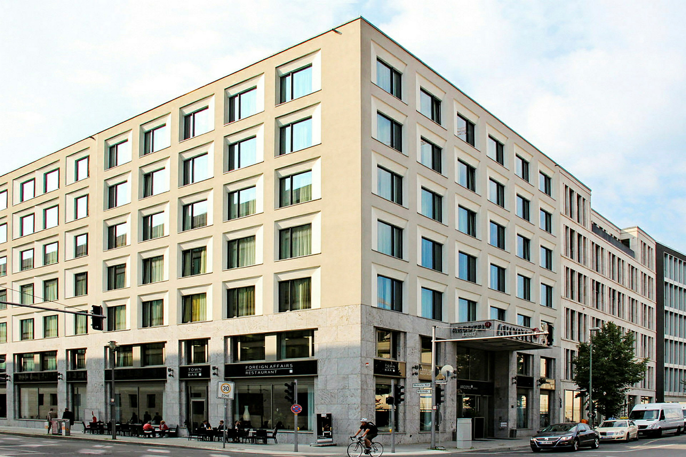 Et hjørnebygg med moderne fasader og store vinduer, med restaurant og bar i første etasje. (AI-generert tekst)