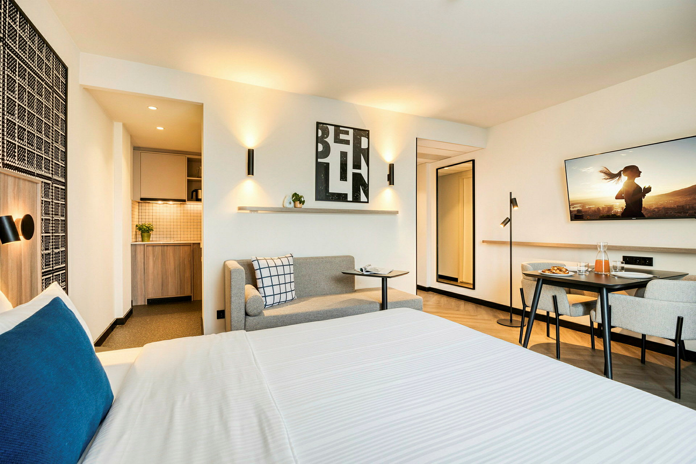 Interiør av et moderne hotellrom med seng, liten kjøkkenkrok og sittegruppe. (AI-generert tekst)