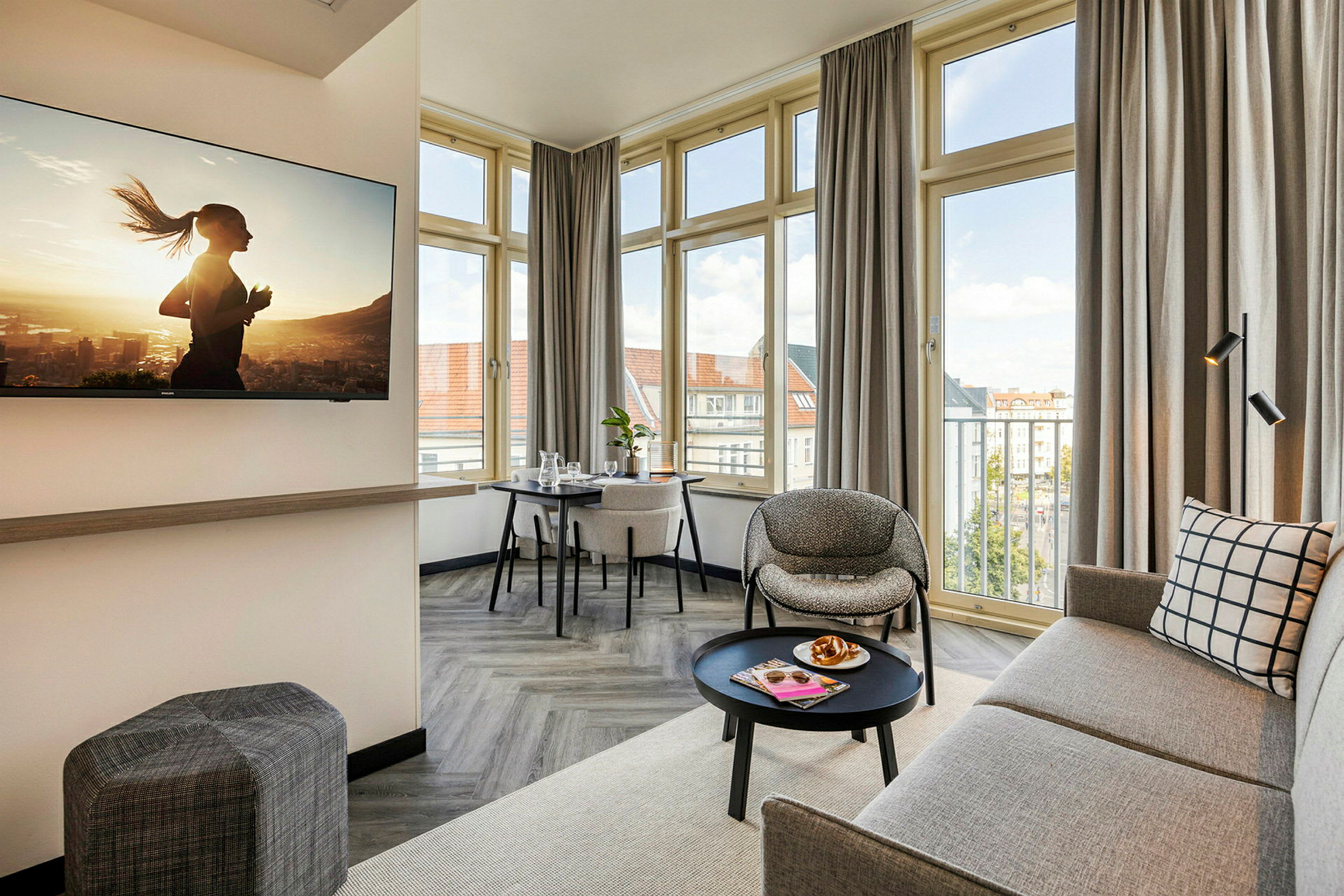 En moderne og lys hotellsuite med sofa, lenestol, bord og en TV på veggen. (AI-generert tekst)