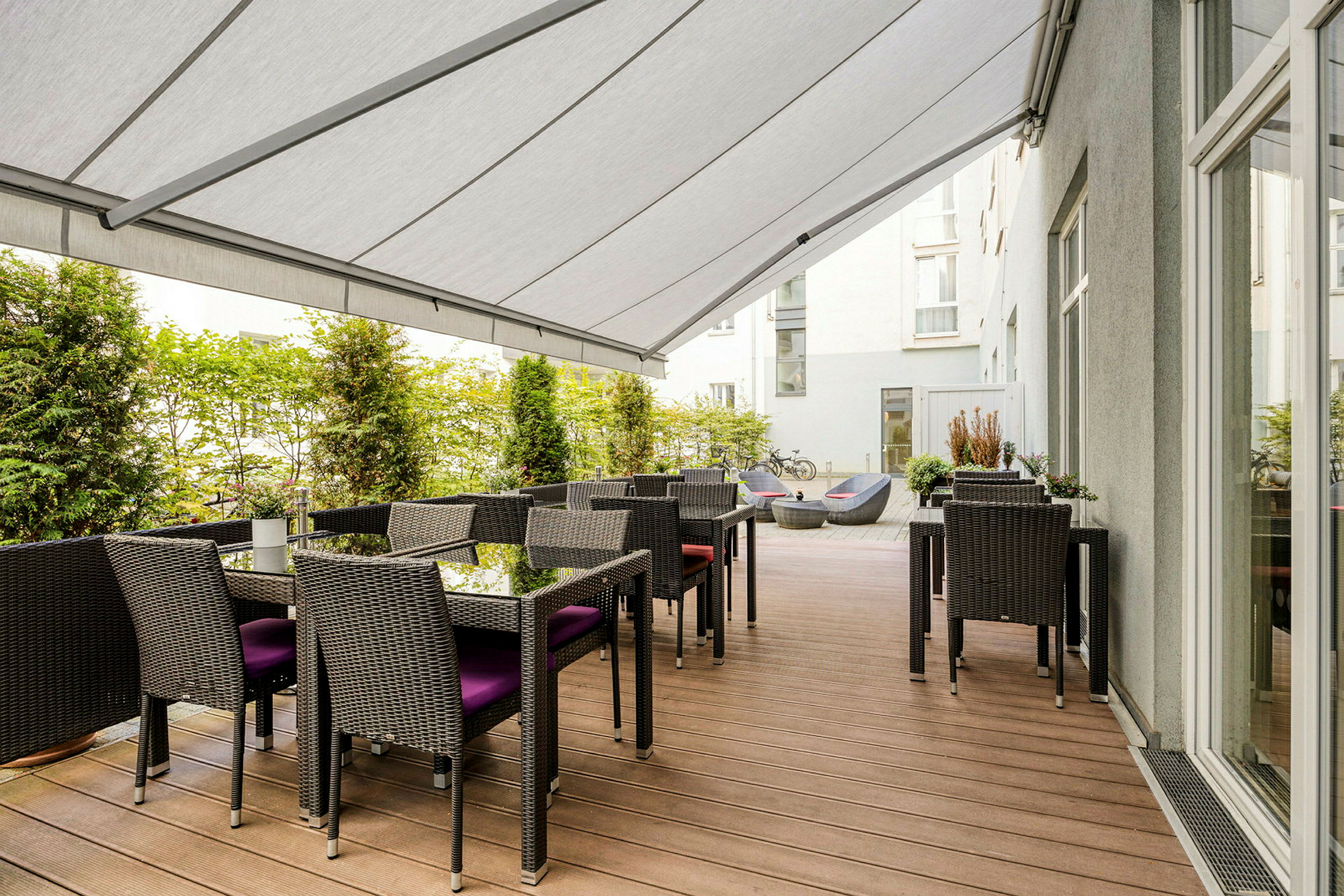 En terrasse med bord, stoler og en overhengende markise. (AI-generert tekst)