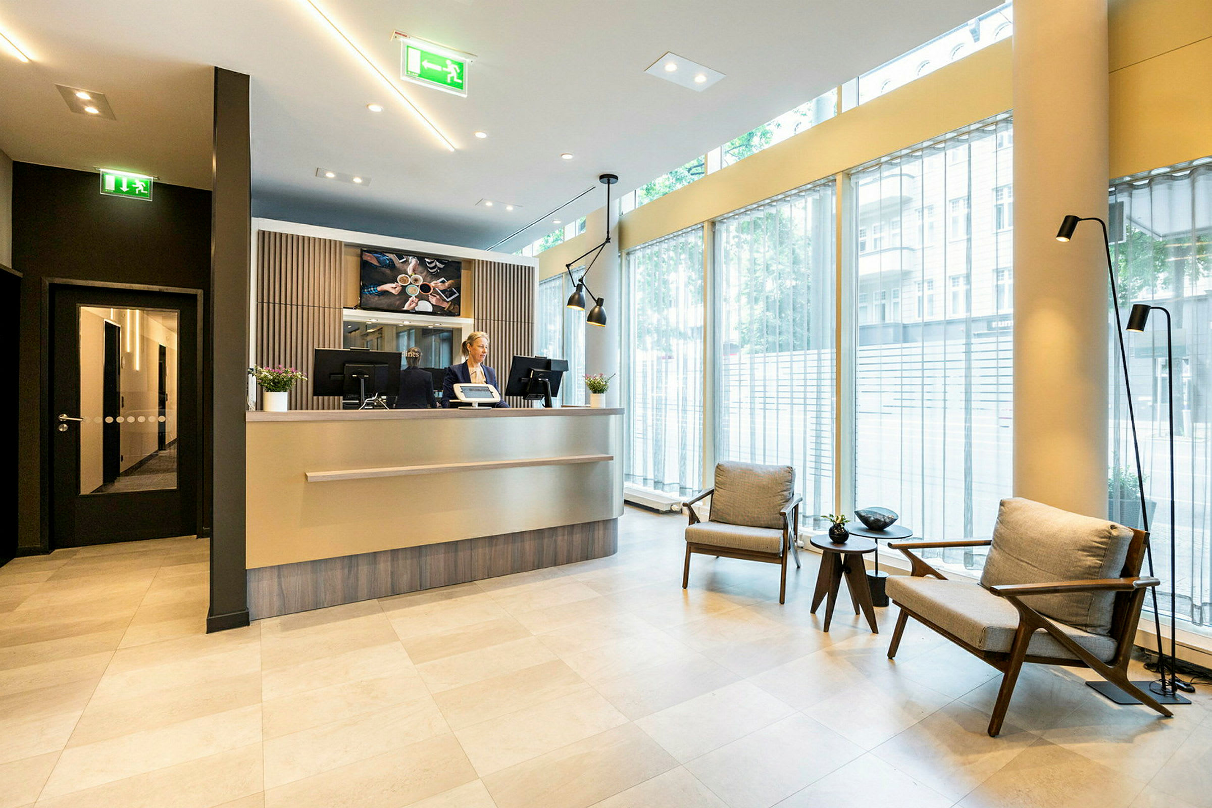 Hotellobby med resepsjon og sitteområde, store vinduer. (AI-generert tekst)