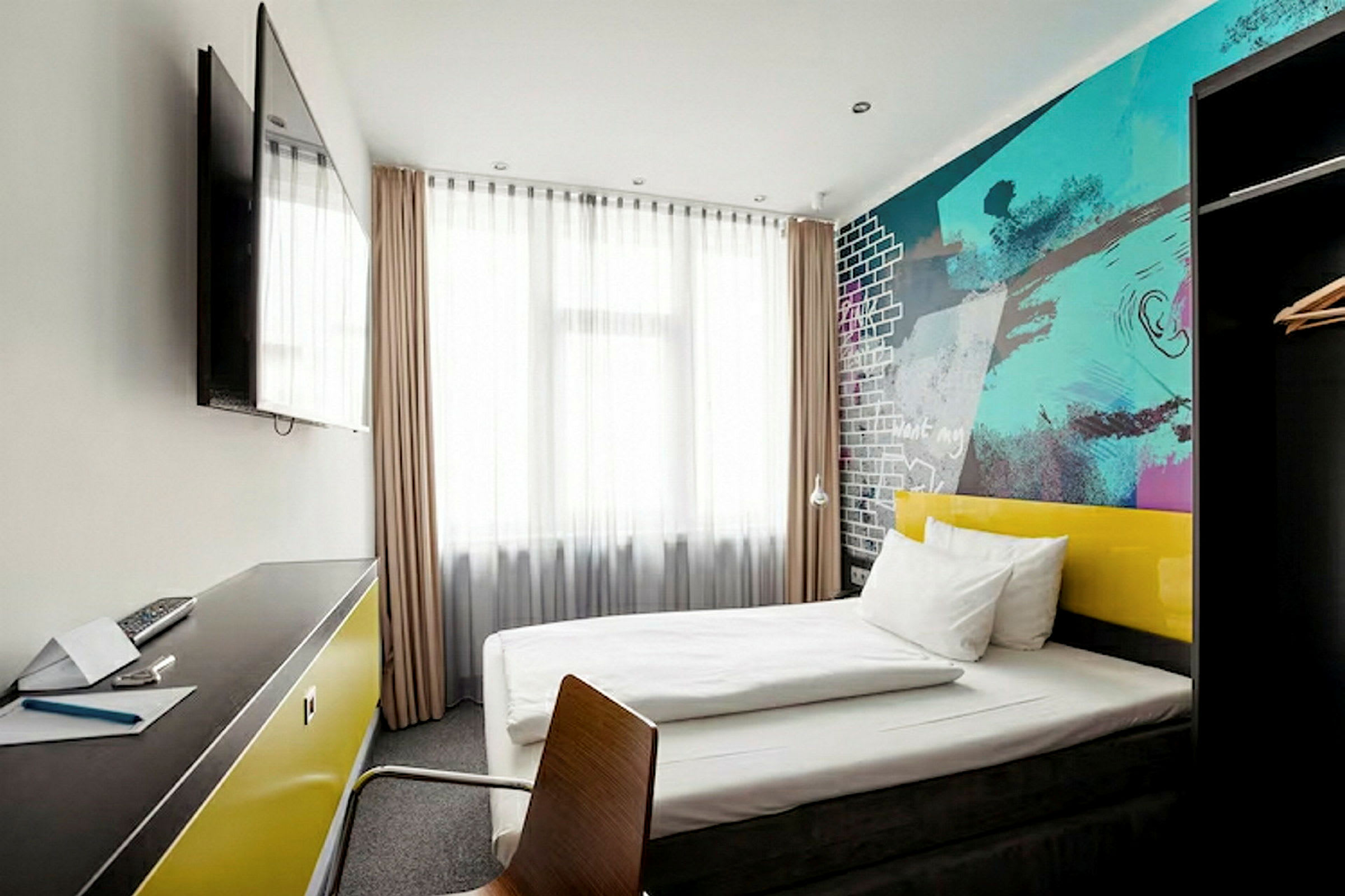 Et moderne hotellrom med en seng, fargerike vegger og et skrivebord med en TV på veggen. (AI-generert tekst)