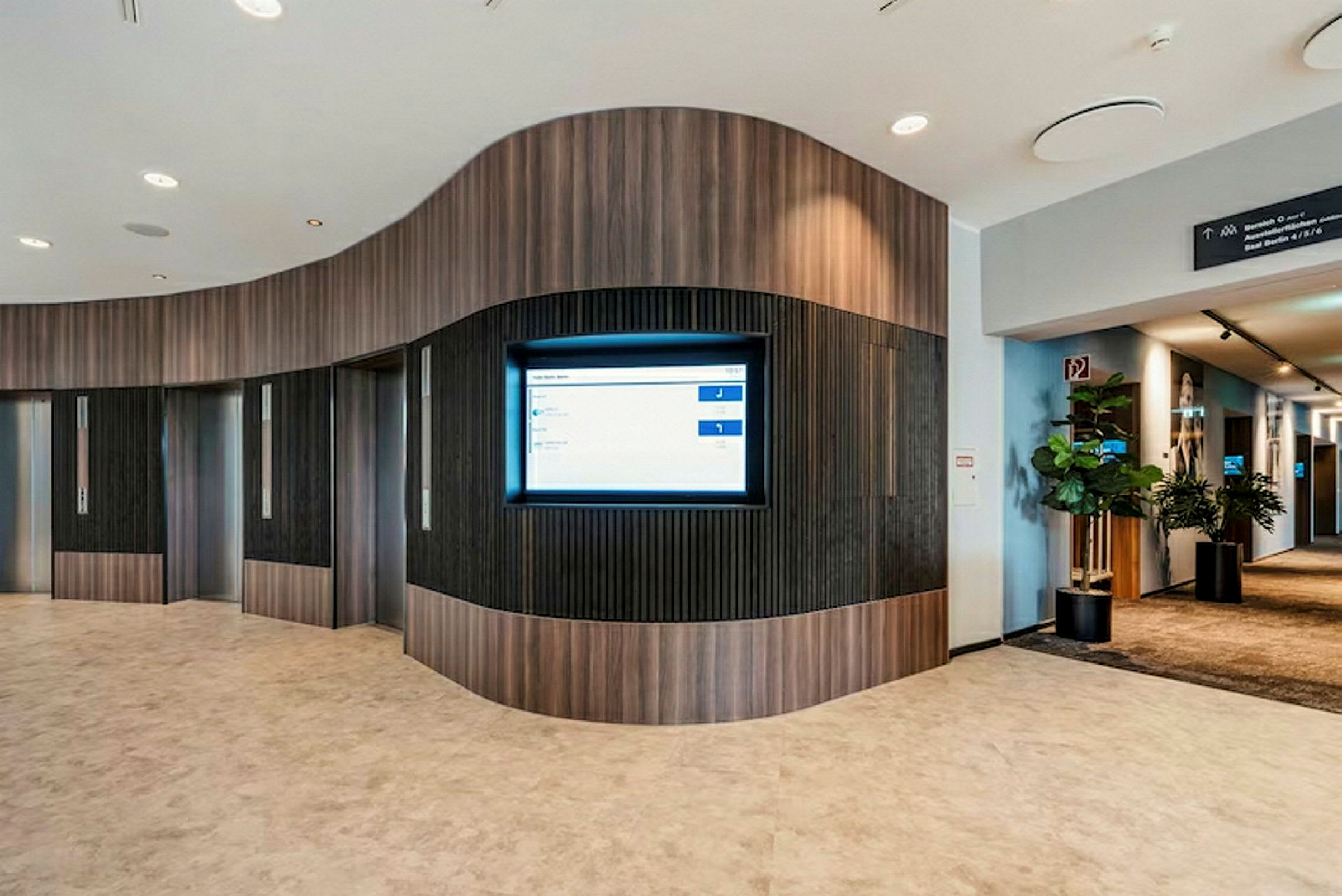 Interiør av en moderne lobby med heiser og en informasjonsskjerm på veggen. (AI-generert tekst)