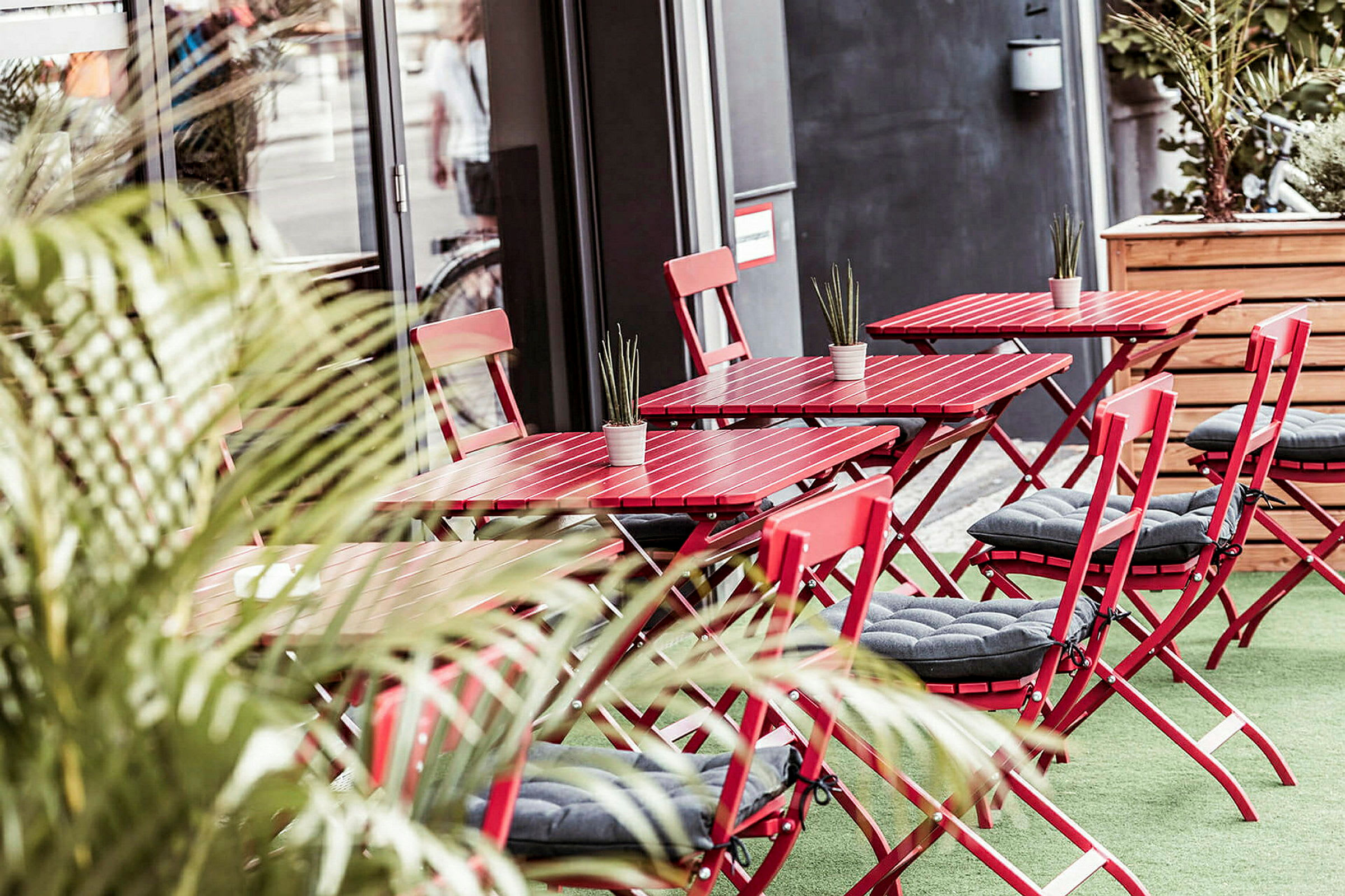 Bilde av en uterestaurant med røde bord og stoler samt små plantepynt. (AI-generert tekst)