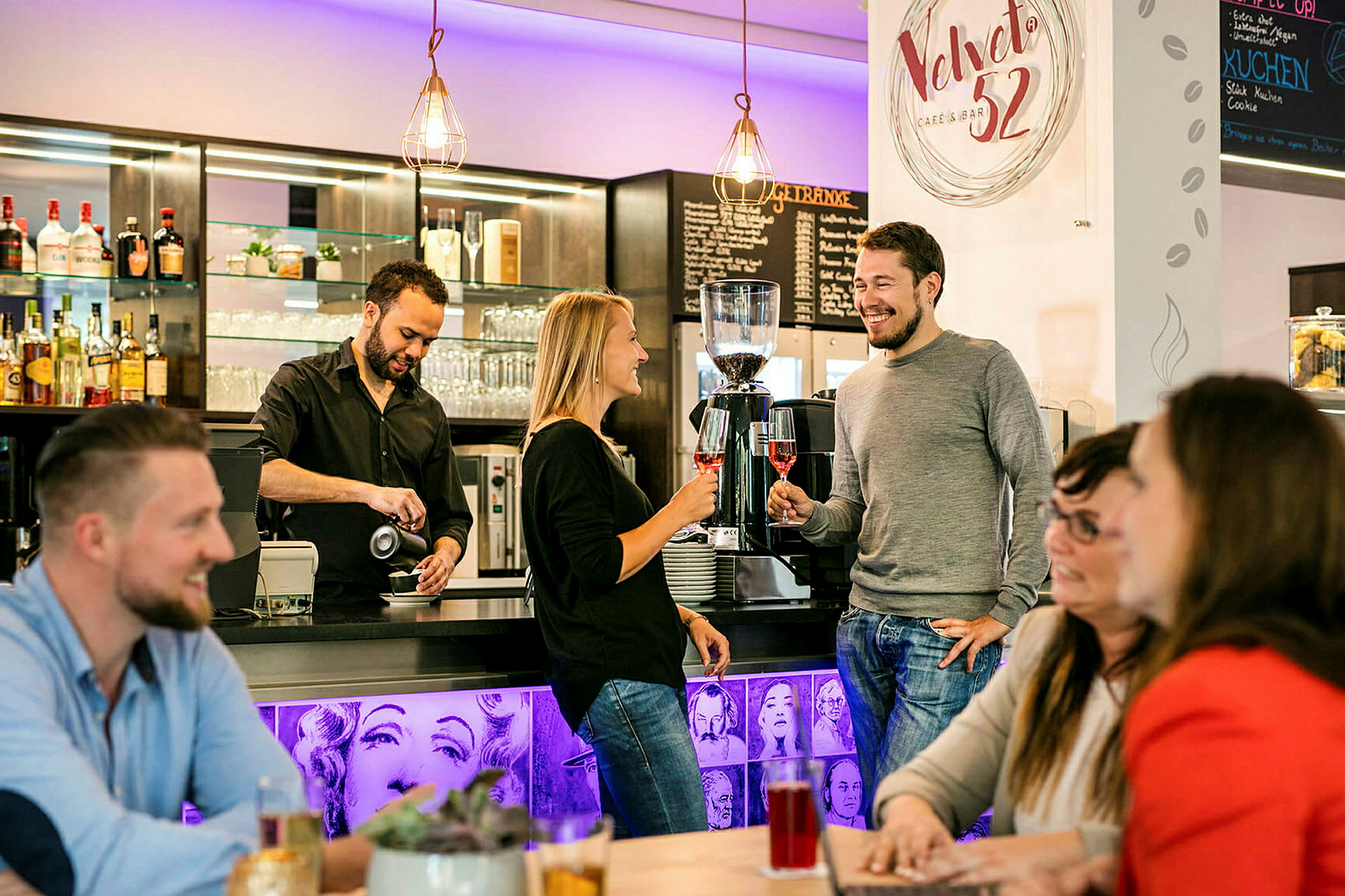 En barista heller kaffe ved en bardisk der mennesker står og sitter og nyter sine drikker. (AI-generert tekst)