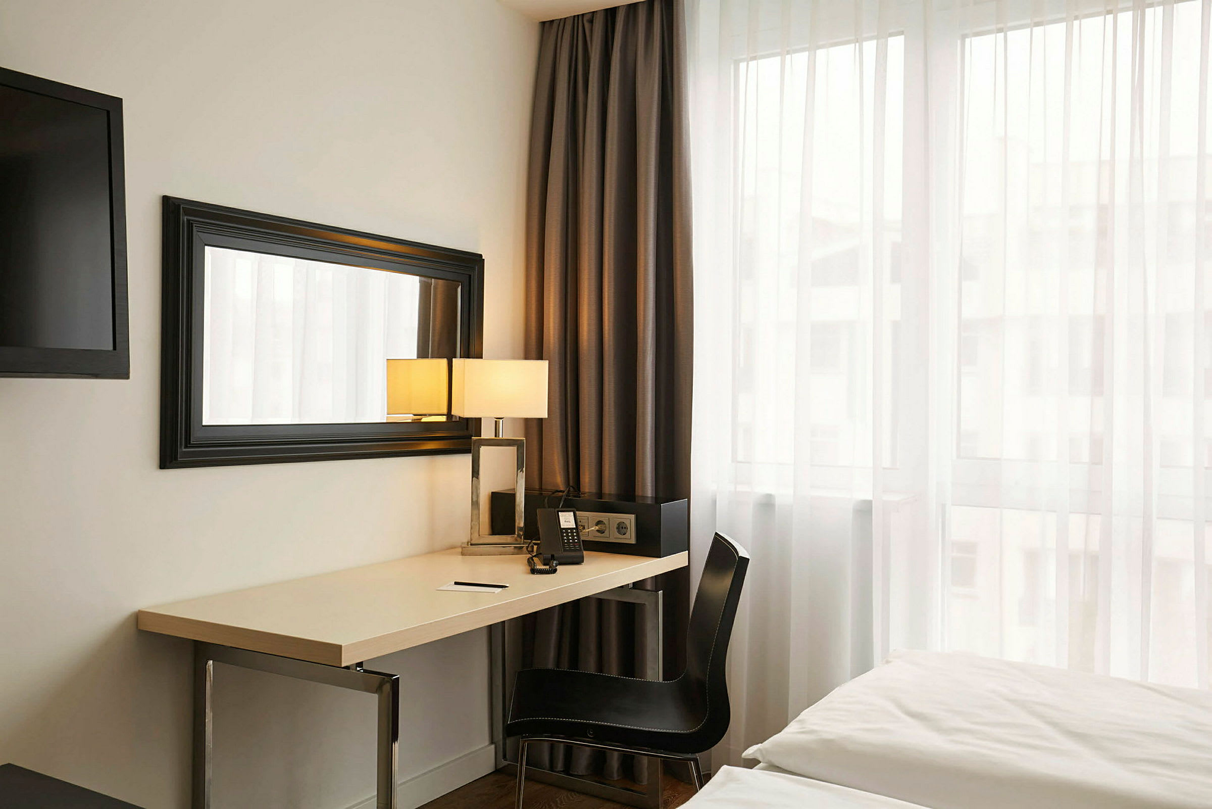 Et hotellrom med skrivebord, speil, seng og et vindu. (AI-generert tekst)