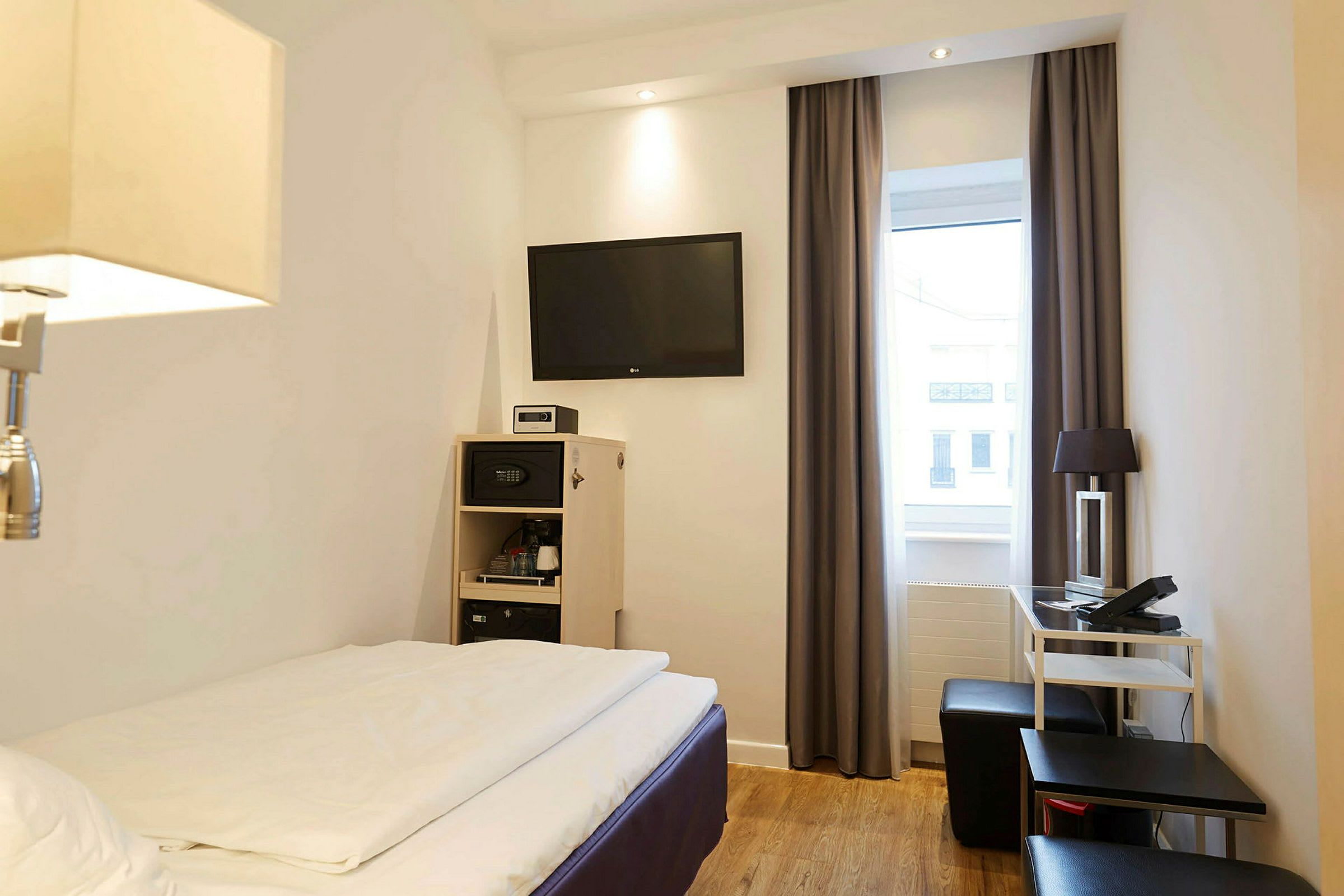 Et hotellrom med en seng, TV på veggen og møbler som et skrivebord og stol. (AI-generert tekst)