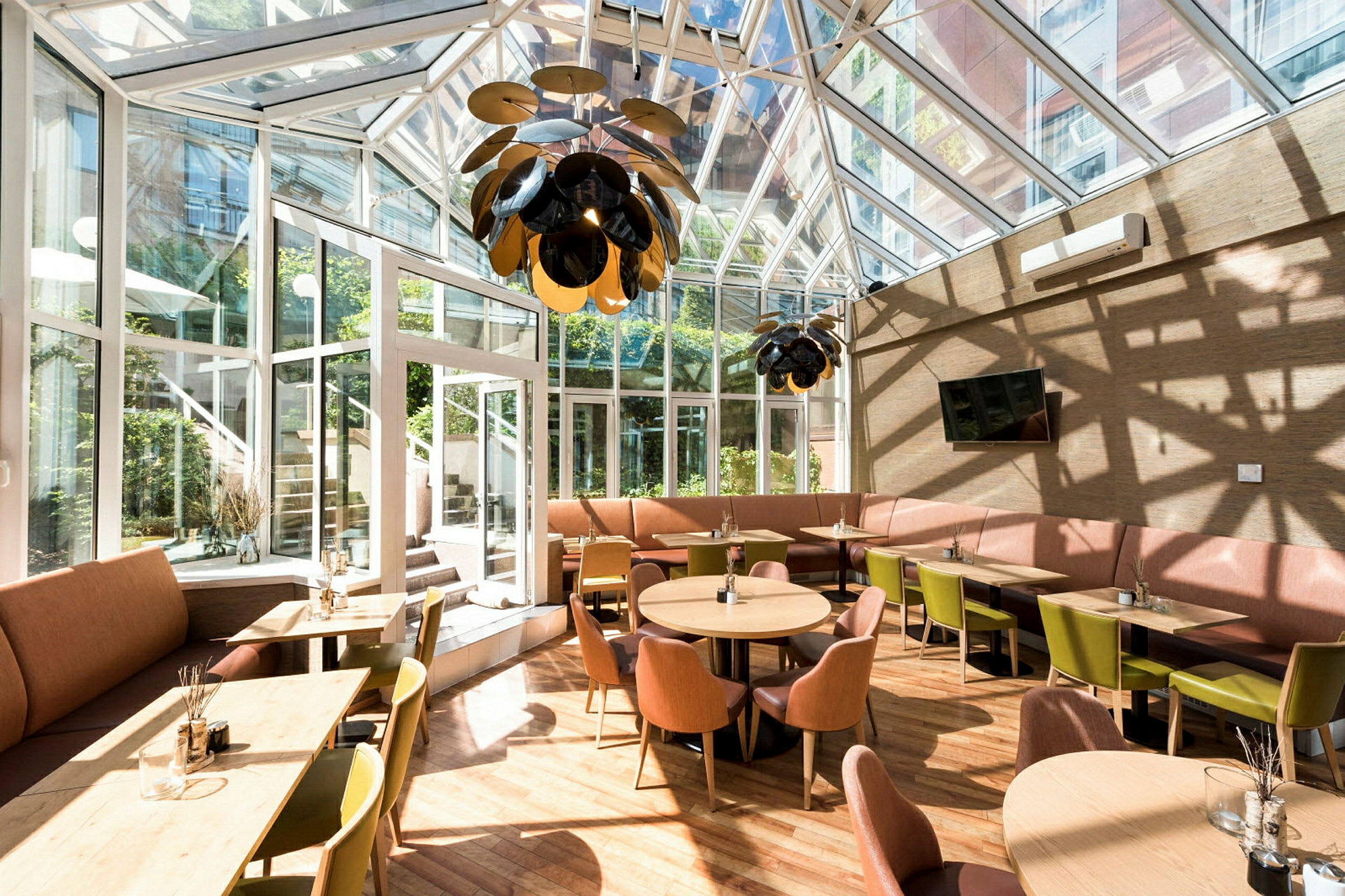 En lyst møblert kafé med store vinduer og tak i glass. (AI-generert tekst)