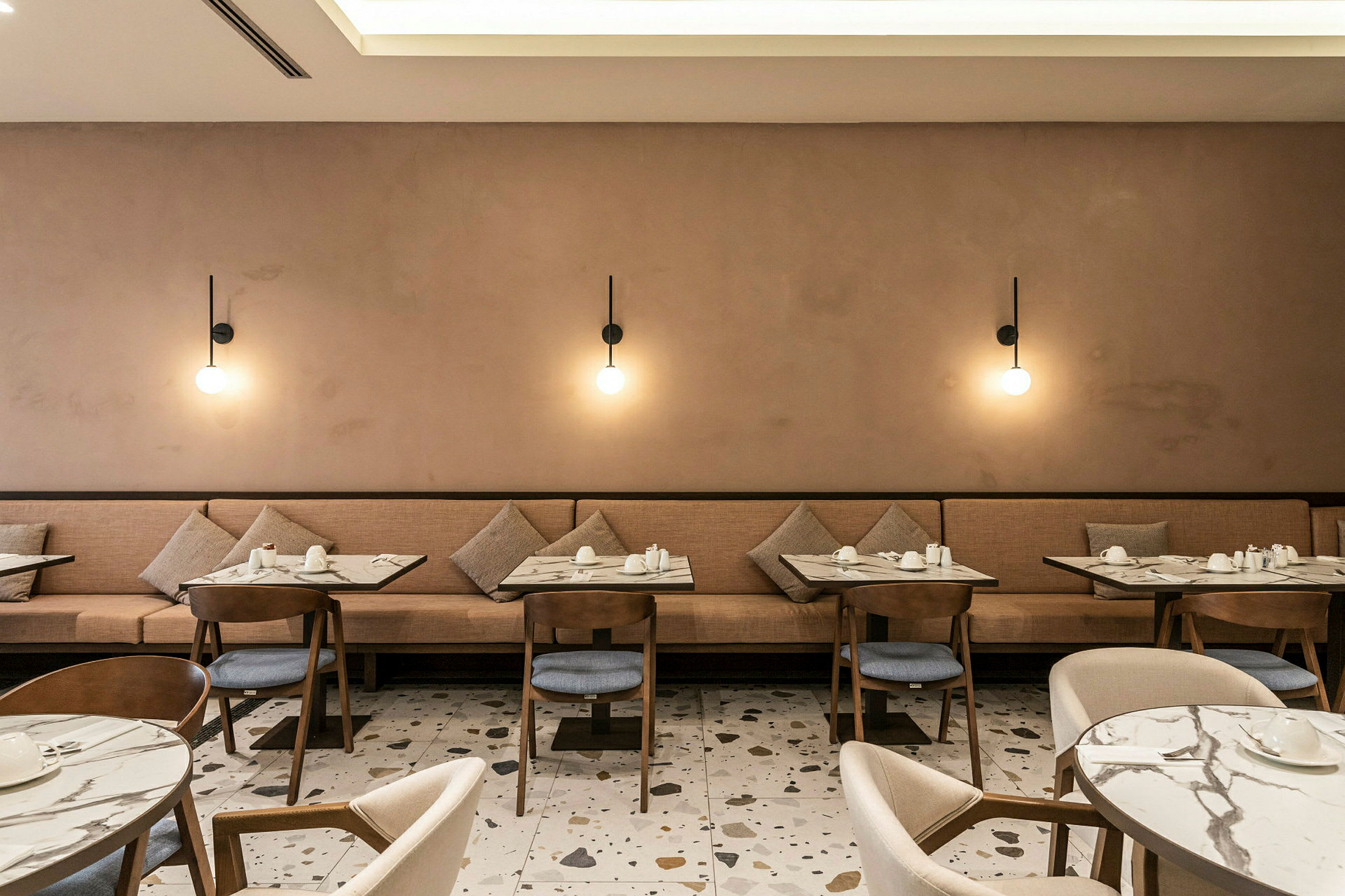 Restaurant med bord og stoler, samt beige sofa og vegglamper. (AI-generert tekst)