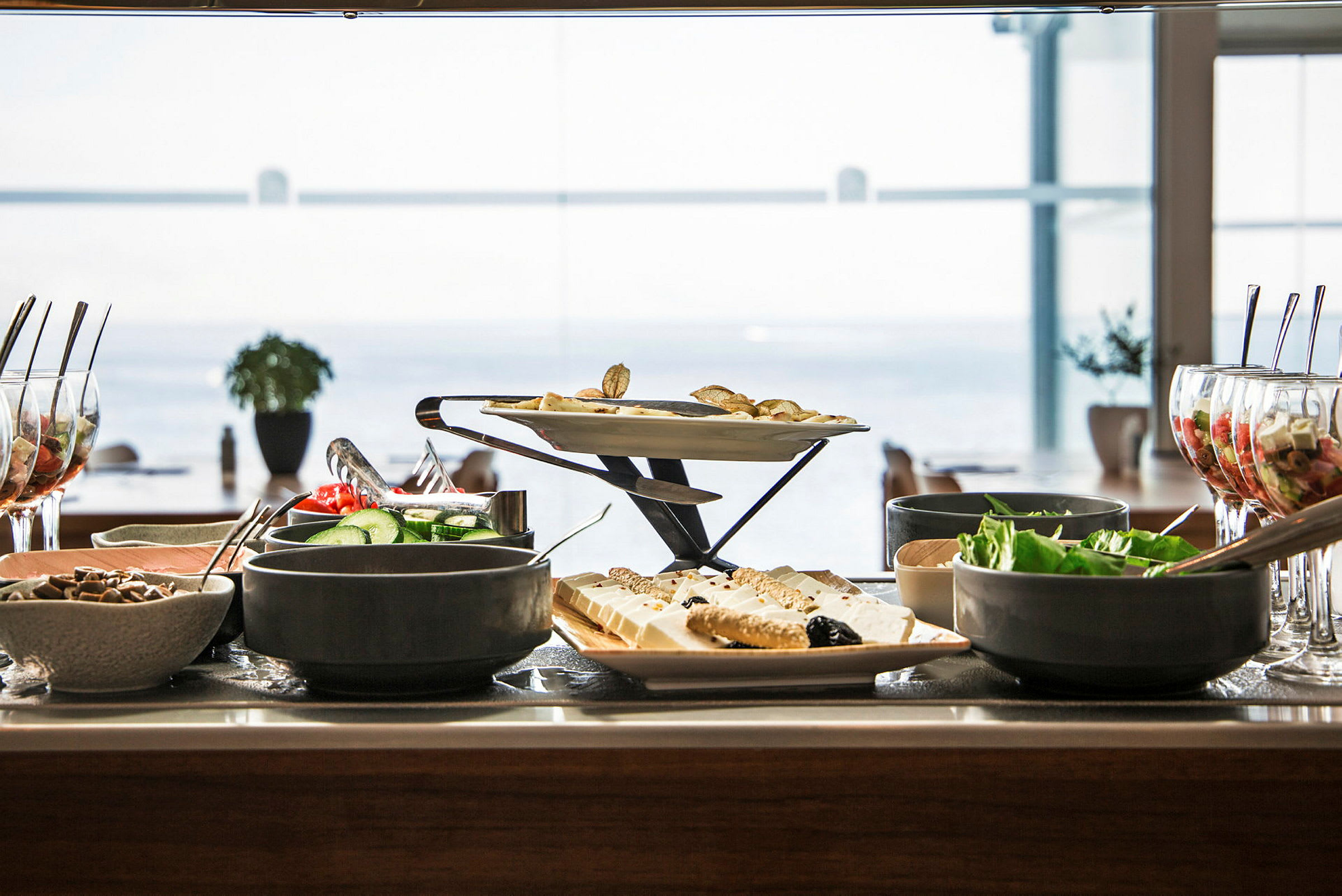 Buffet med forskjellige retter, salater og desserter på et bord med havutsikt i bakgrunnen. (AI-generert tekst)