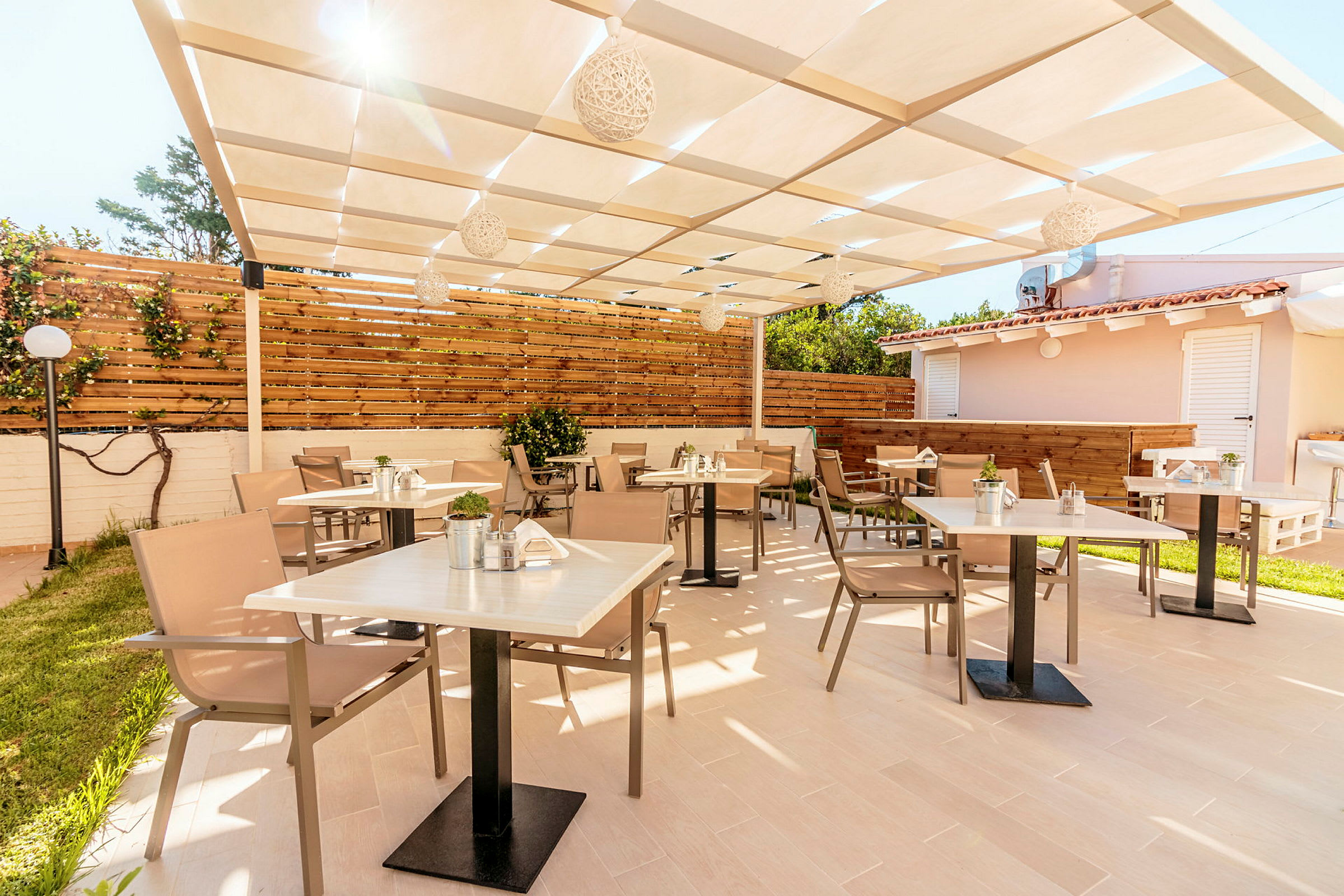 En utendørs terrasse med bord og stoler under et skyggefullt tak. (AI-generert tekst)