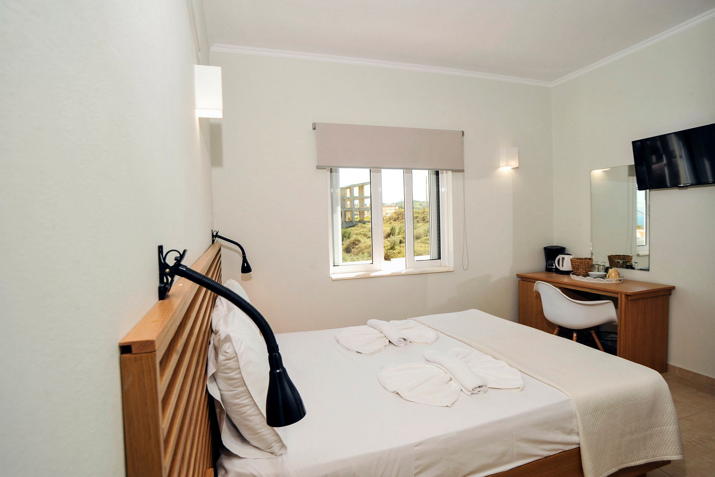 Et hotellrom med en seng, vindu, skrivebord, stol og TV. (AI-generert tekst)