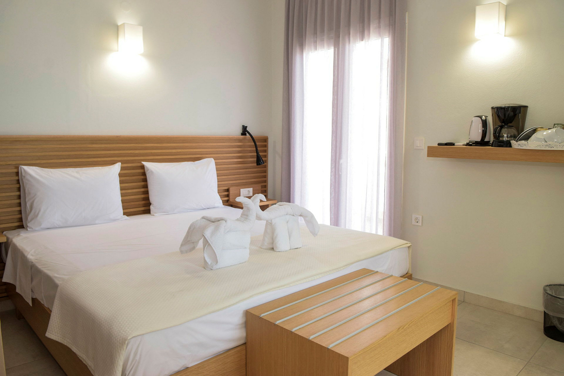 Hotellrom med en dobbeltseng med hvite laken og svaneformede håndklær, samt en hylle med kaffetrakter. (AI-generert tekst)
