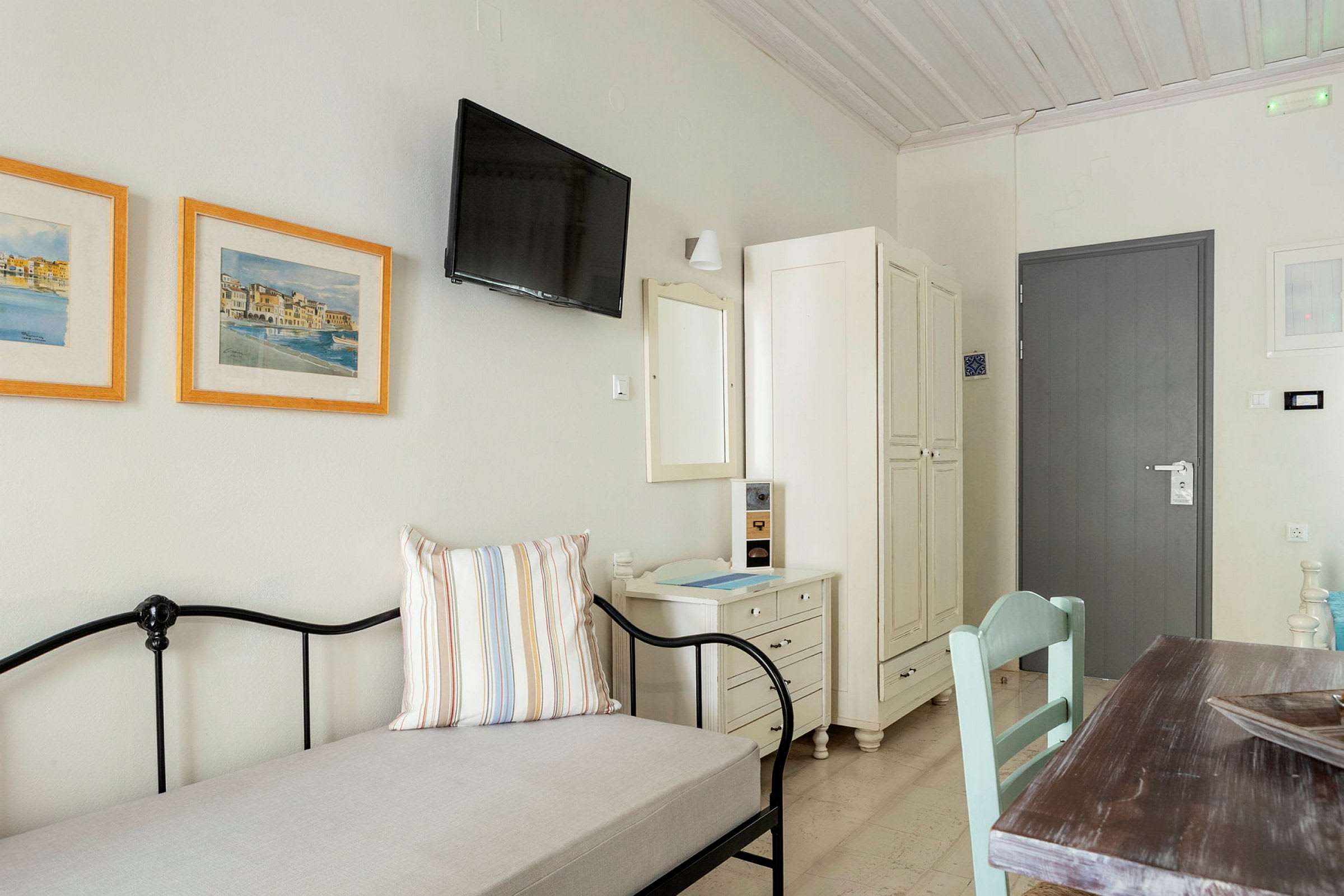 Et lyst og enkelt møblert hotellrom med en dør, garderobe, bilder og bord. (AI-generert tekst)