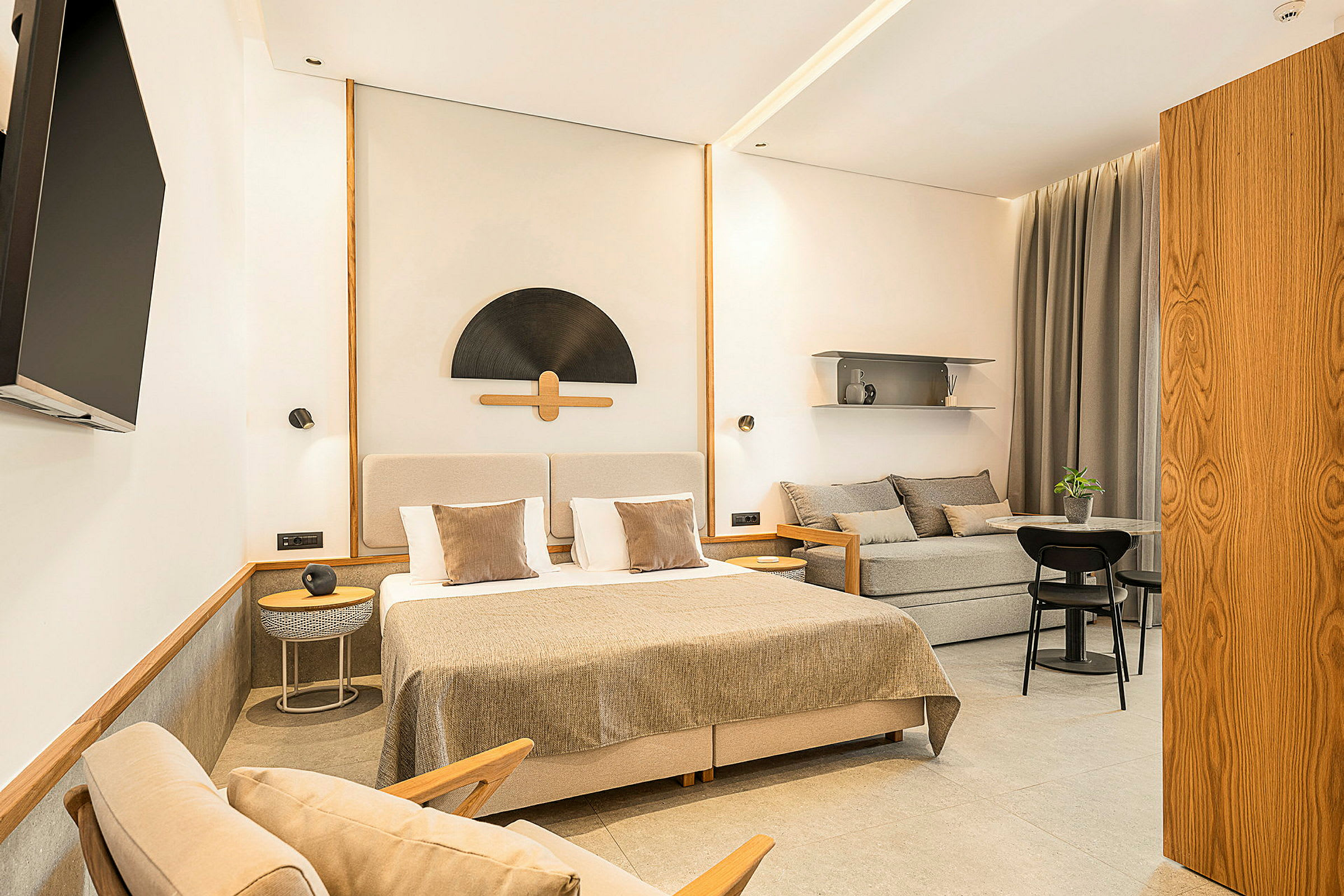 Et stilrent hotellrom med en dobbeltseng, sofa, bord og en veggmontert TV. (AI-generert tekst)