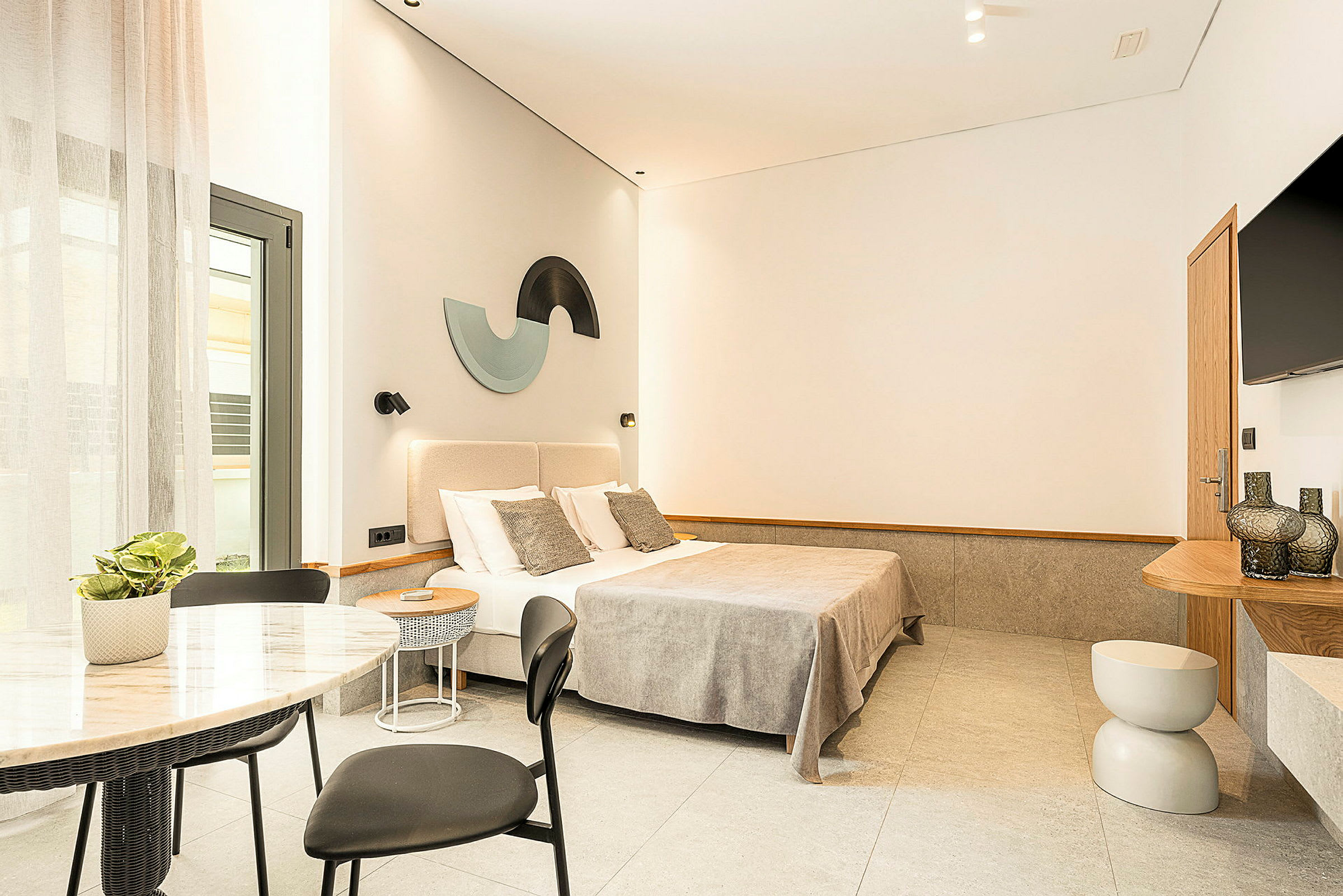 Et moderne og stilrent hotellrom med en dobbeltseng, garderobe, bord med stoler samt dekorasjoner på veggene. (AI-generert tekst)