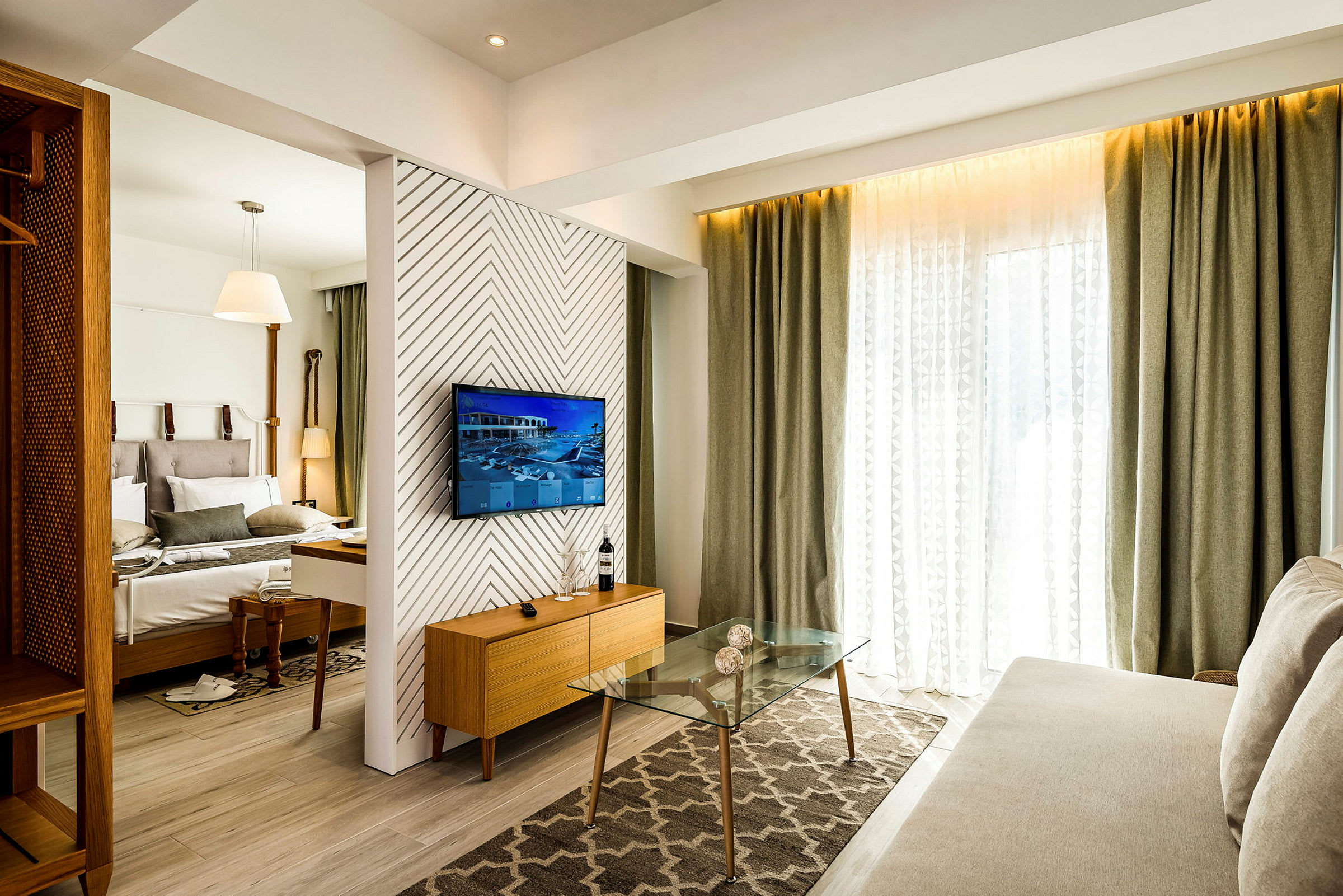 Et hotellrom med moderne møbler, inkludert en seng, en sofa, et glassbord og en TV på veggen. (AI-generert tekst)