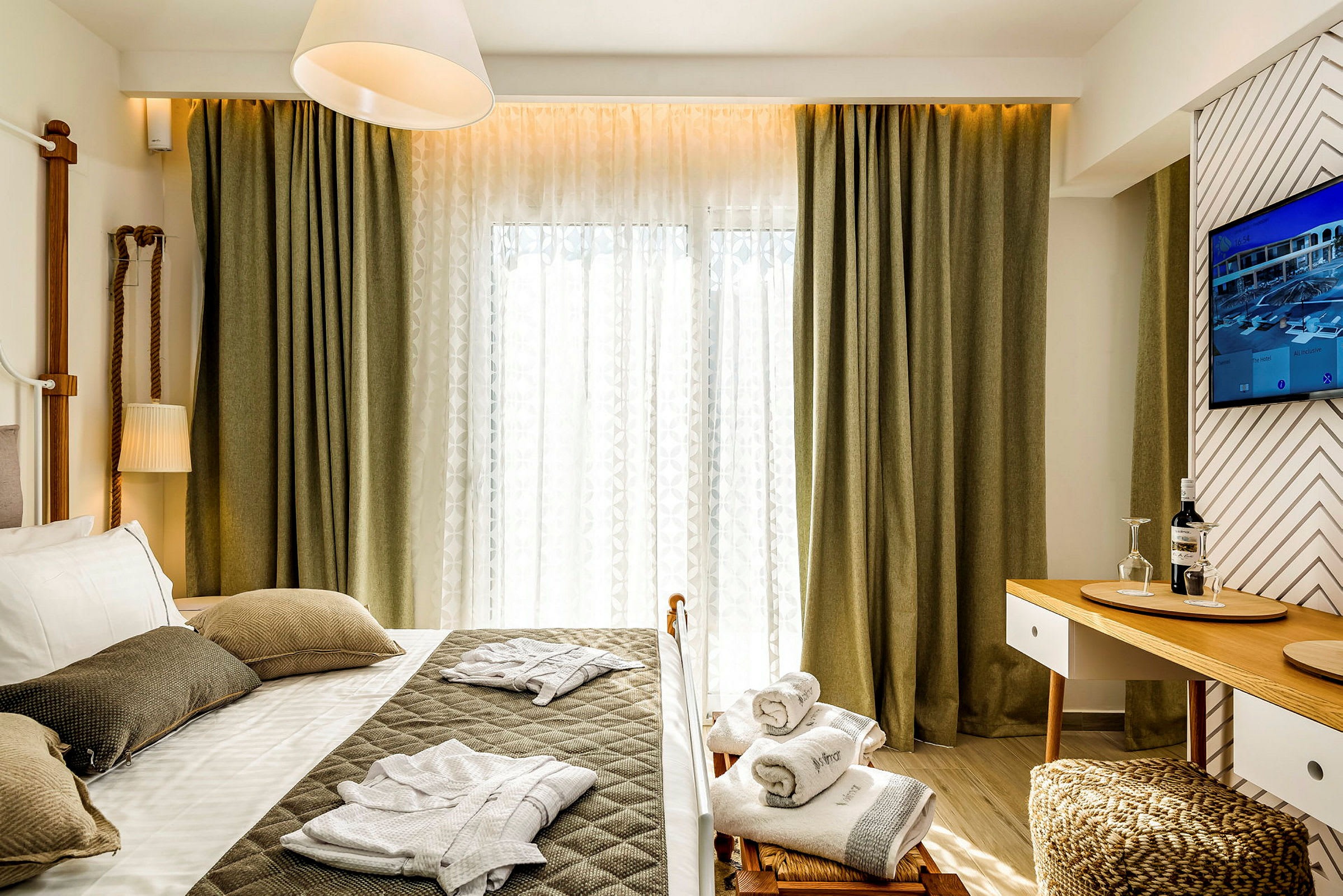 Et hotellrom med en seng, pynteputer og sammenlagte badekåper. Det er et bord med glass og en flaske. (AI-generert tekst)
