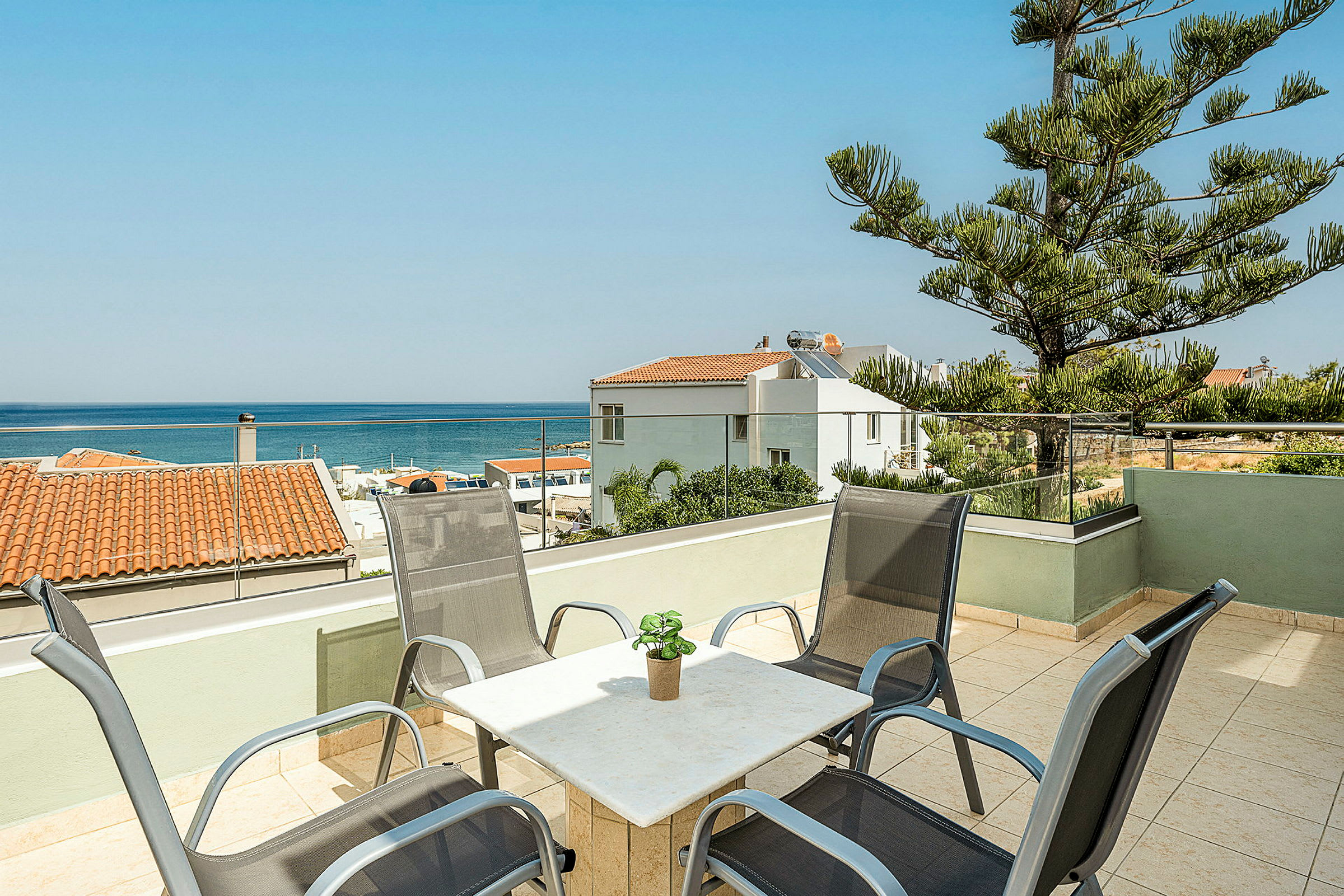 En terrasse med stoler og bord samt utsikt over havet og omkringliggende hus. (AI-generert tekst)