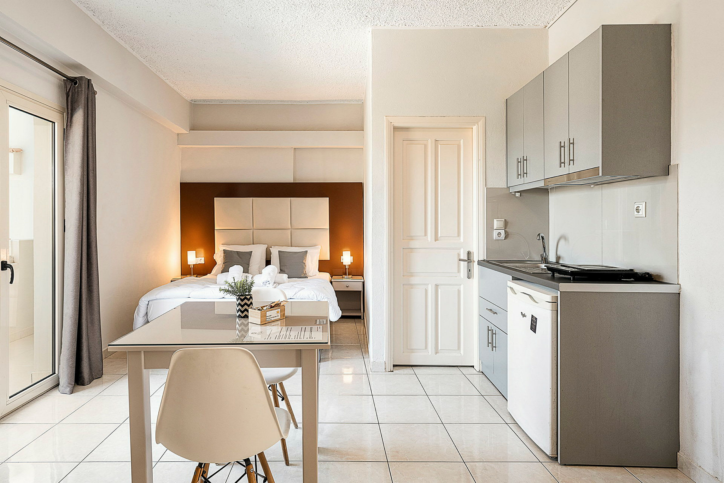 Et lyst og moderne hotellrom med dobbeltseng, et lite spisebord og en kjøkkenkrok. (AI-generert tekst)