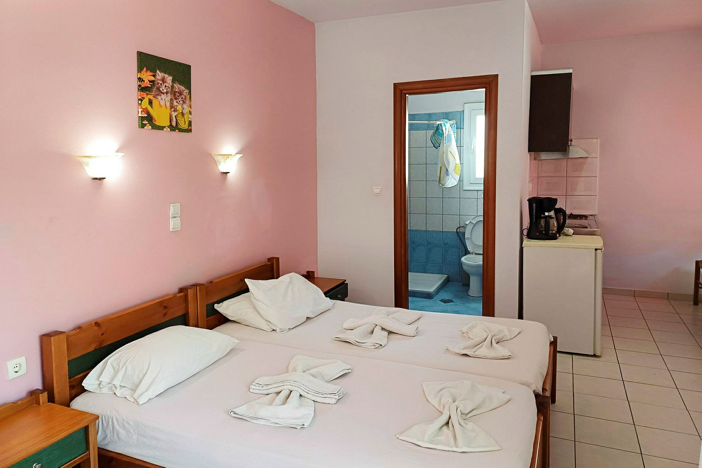 Et enkelt hotellrom med rosa vegger, to enkeltsenger og utsikt mot baderomsdøren. (AI-generert tekst)
