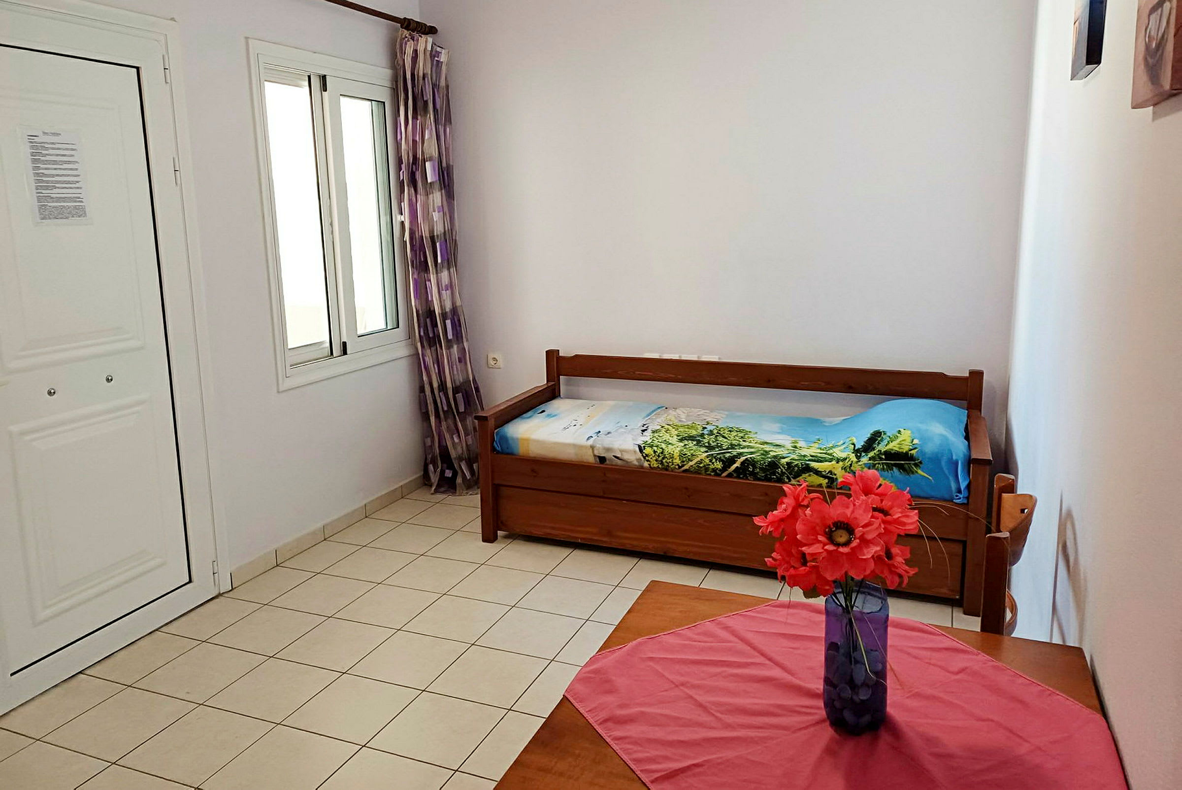 Et rom med en enkeltseng og et bord med en vase med røde blomster. (AI-generert tekst)