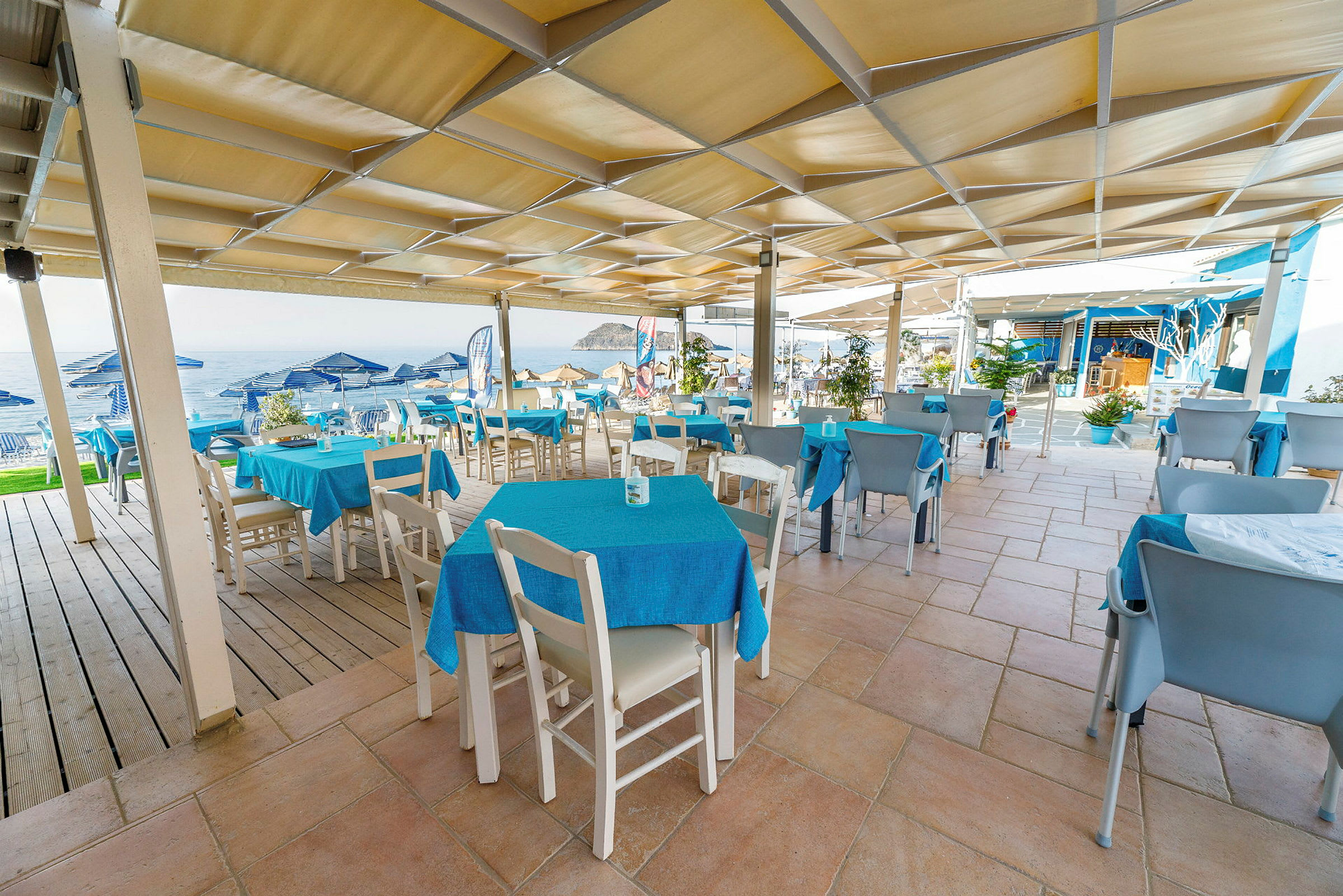 Utendørsrestaurant med blå duker og utsikt mot havet. (AI-generert tekst)