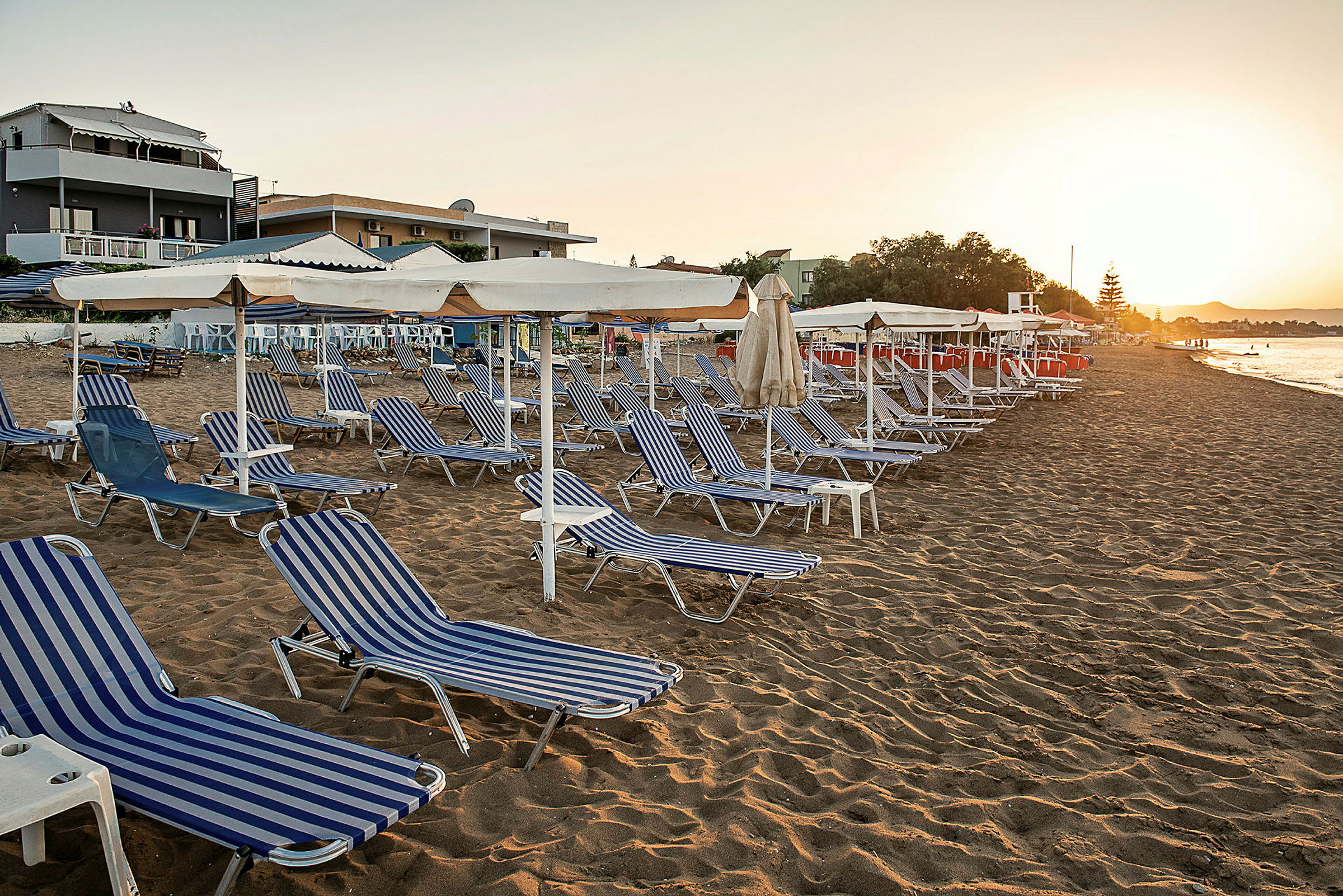 Strand med solsenger og parasoller ved solnedgang. (AI-generert tekst)