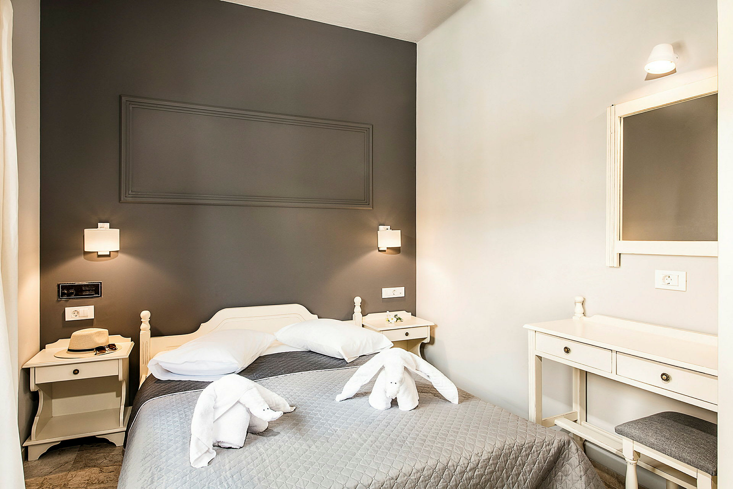 Et hotellrom med en seng, nattbord og speil. Håndklær er brettet som en dekorativ kanin på sengen. (AI-generert tekst)