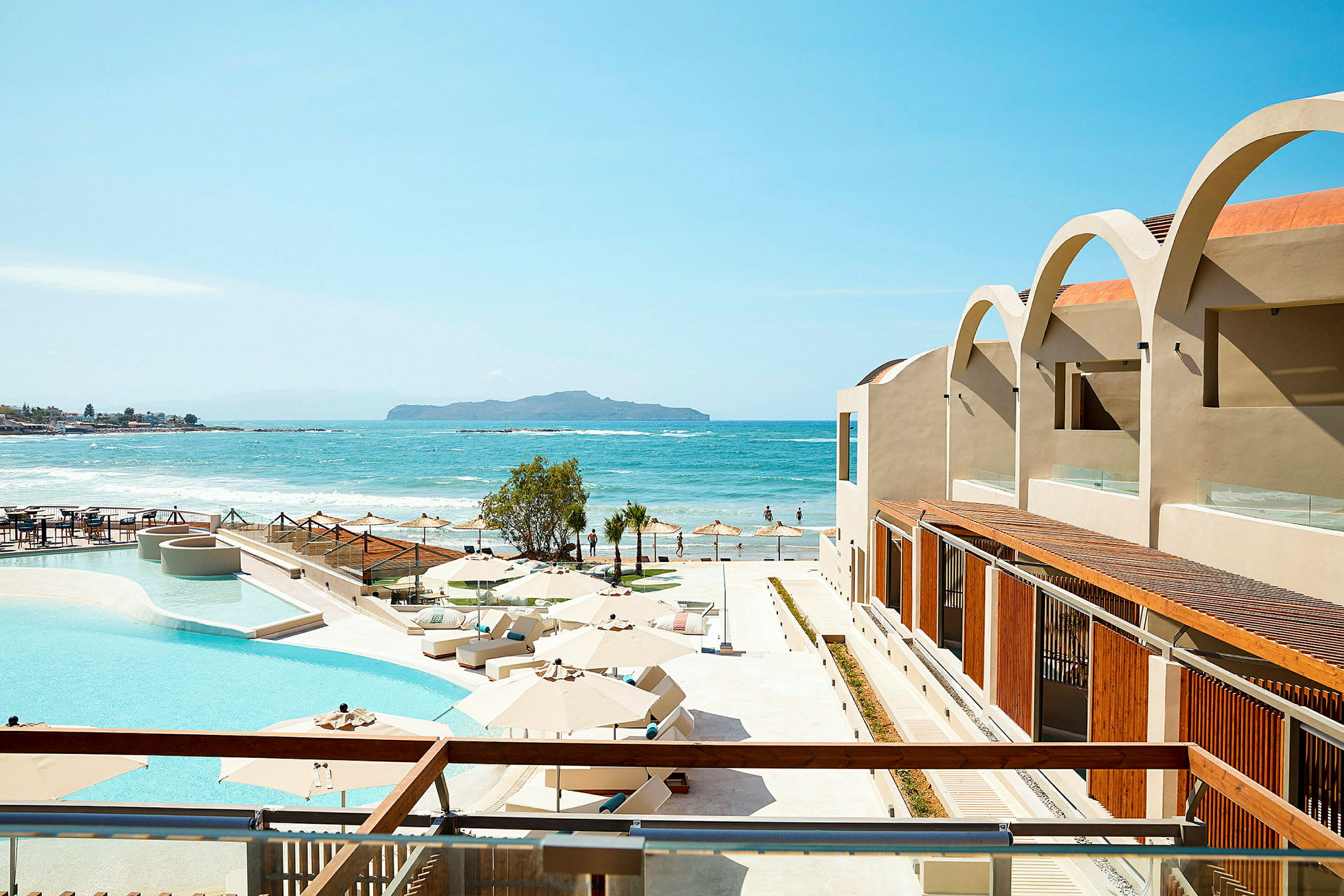 En utsikt over et hotellbasseng og terrasse med utsyn mot havet. (AI-generert tekst)