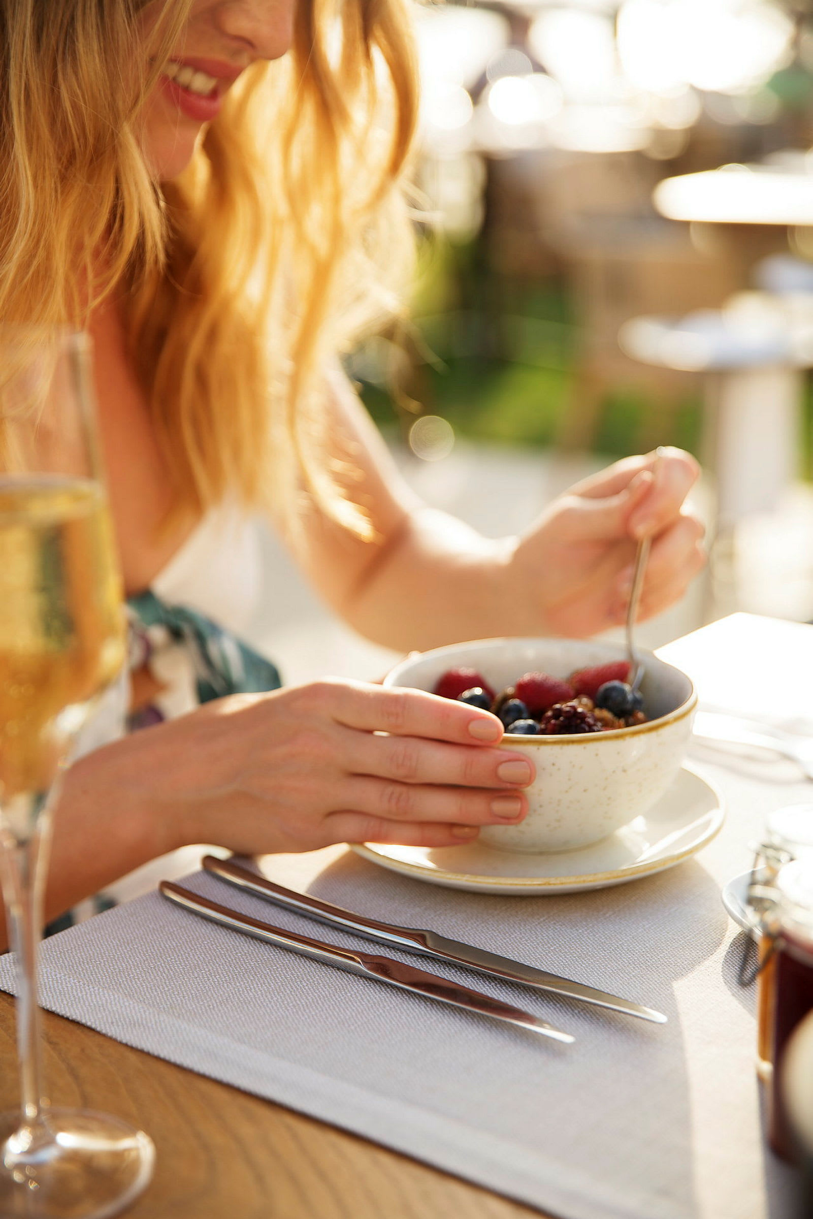 En person spiser frokost med en bolle granola og bær på et bord. (AI-generert tekst)