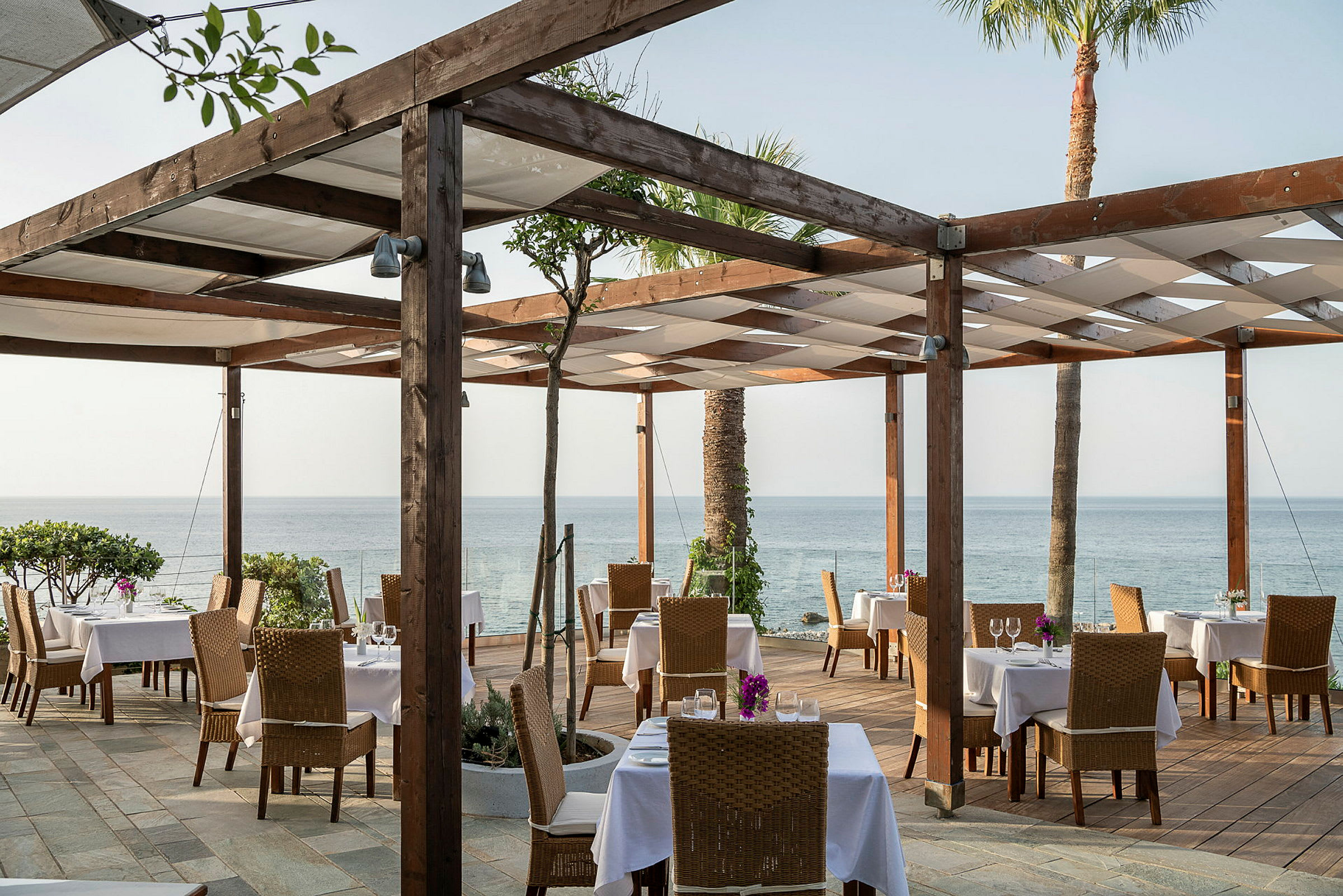 Restaurant med uteservering, bord og stoler, og utsikt over havet. (AI-generert tekst)