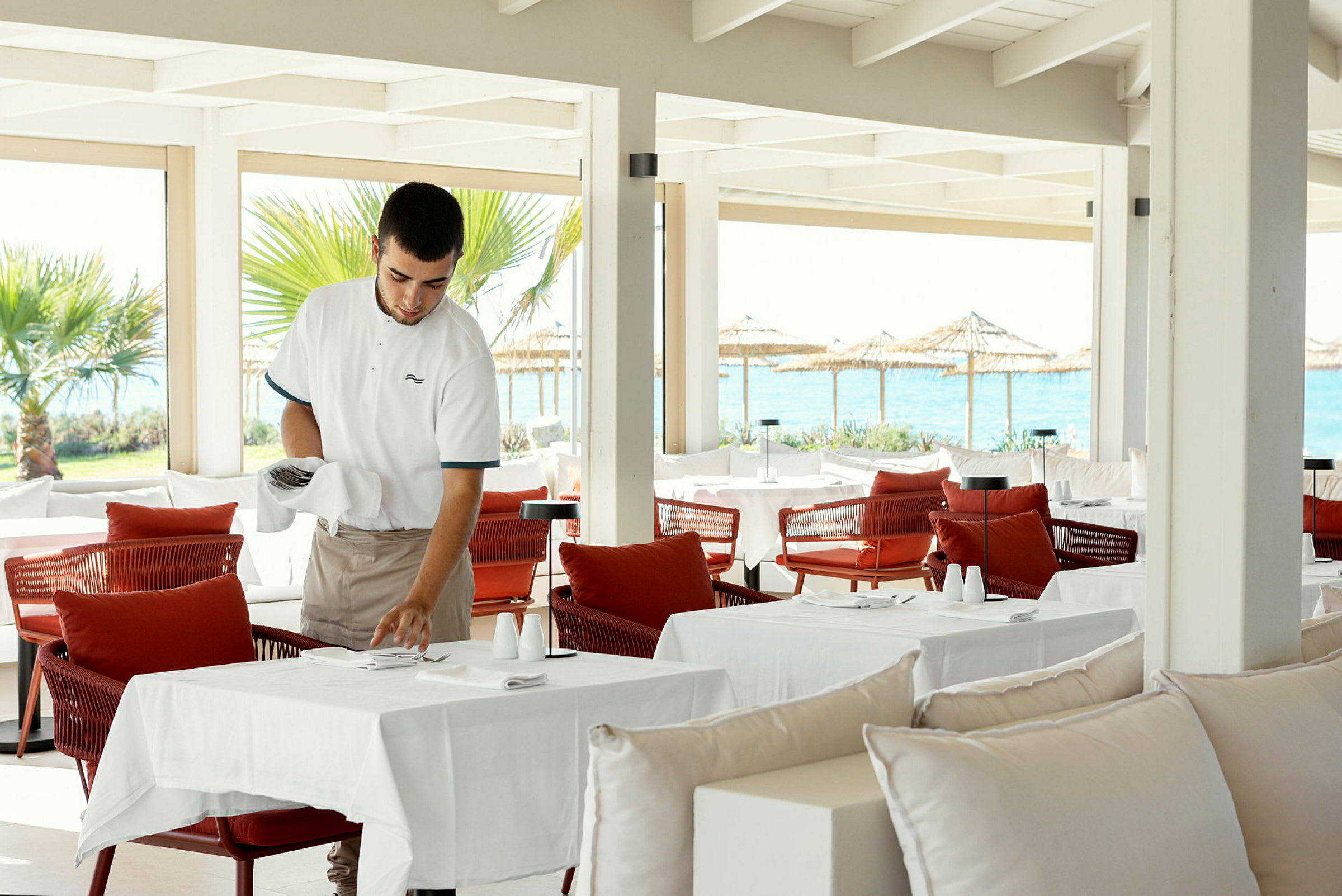Serveringspersonale forbereder bordsetting på en restaurant med havutsikt. (AI-generert tekst)